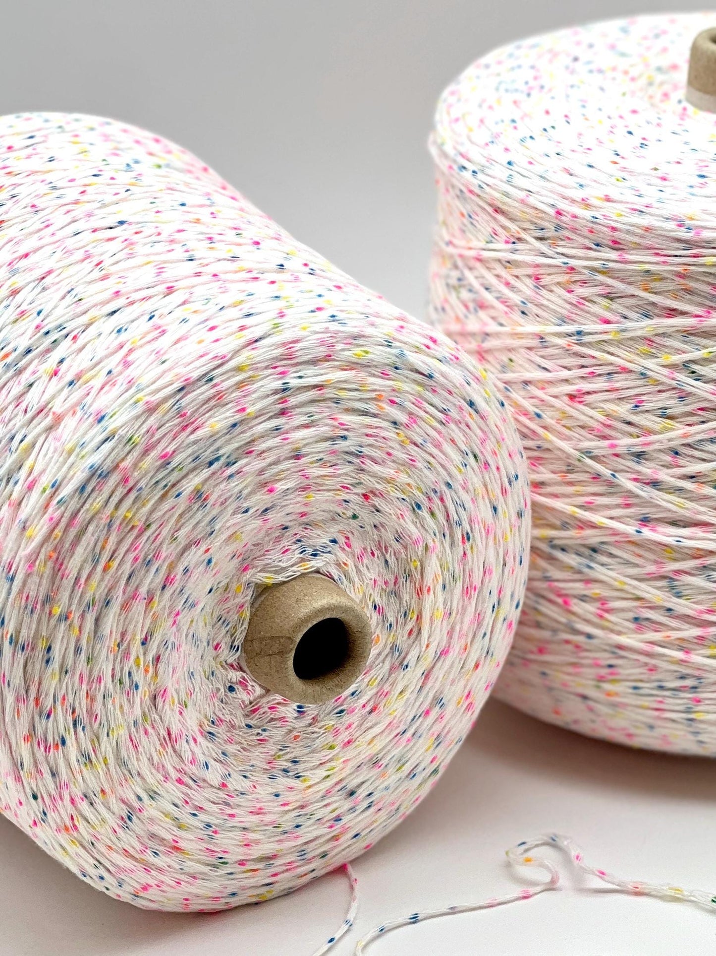 Two spools of multicolored yarn on a light gray background