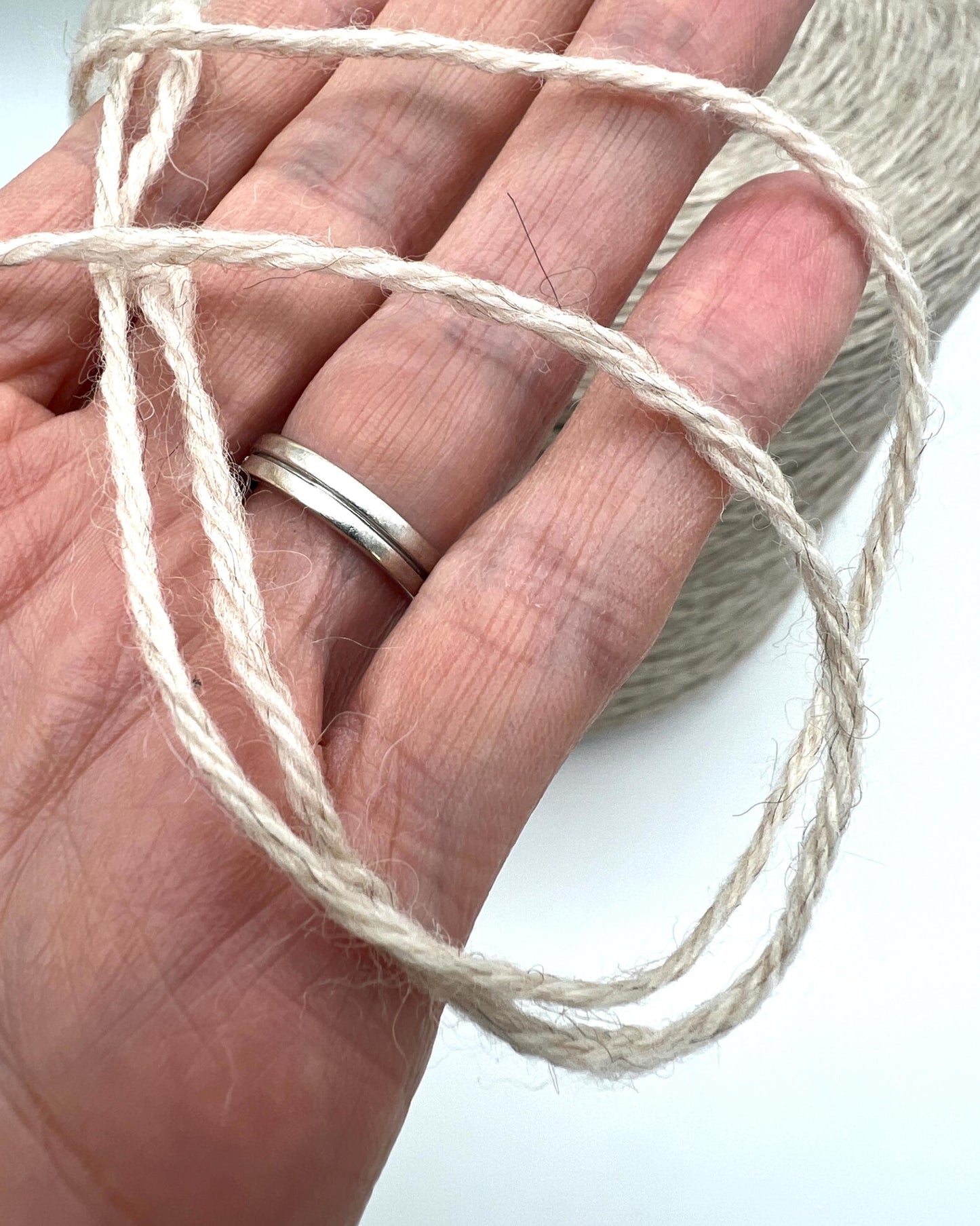 Hand holding a ball of beige yarn with a white background