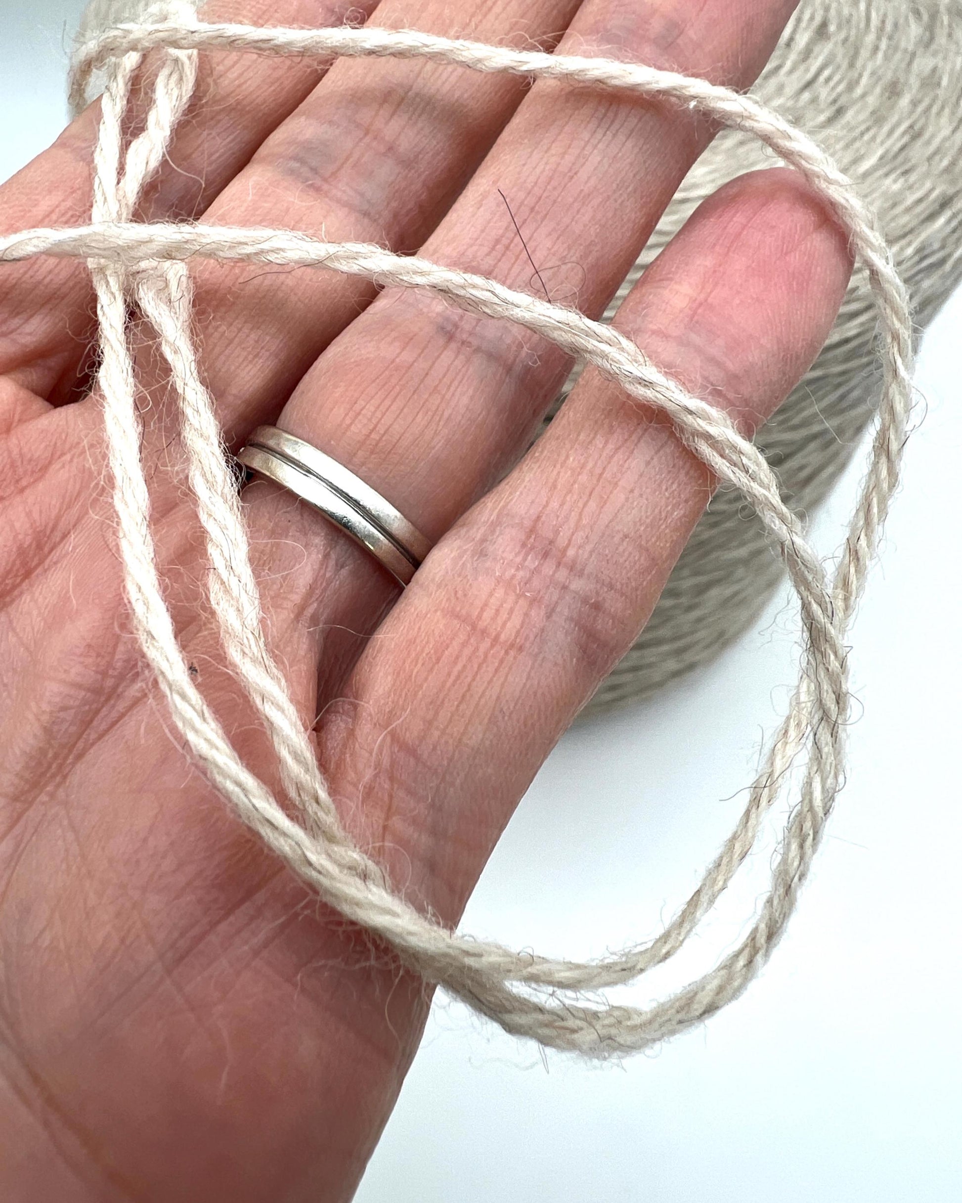 Hand holding a ball of beige yarn with a white background