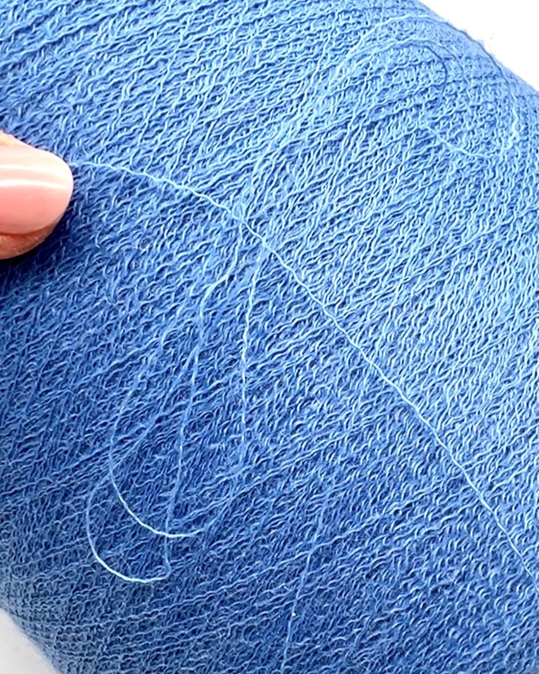 Close-up of a ball of blue yarn with a hand holding it.
