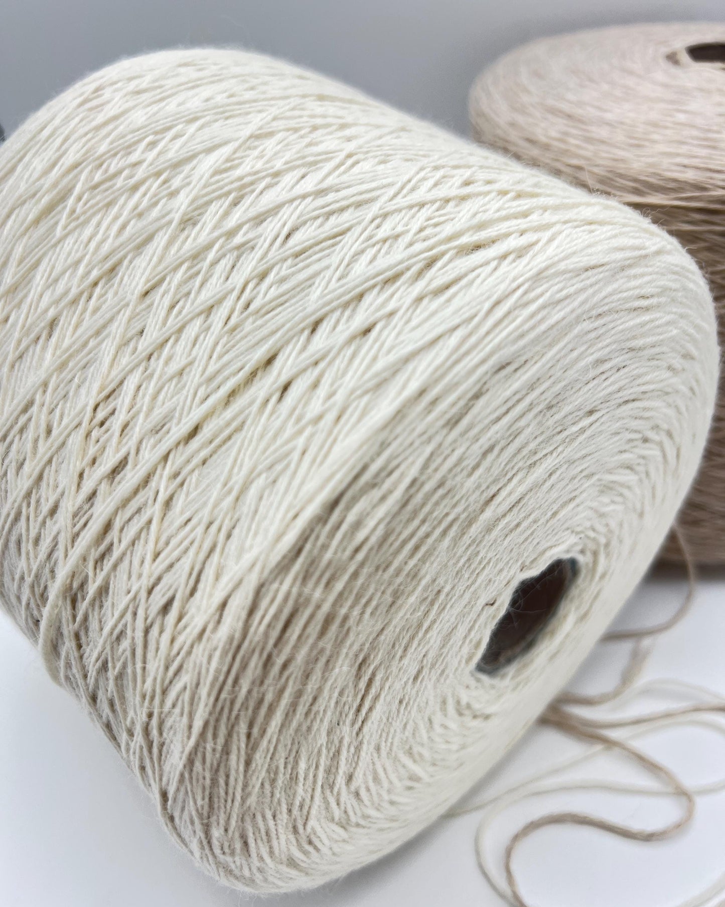 Two spools of yarn, one white and one brown, on a light gray background.