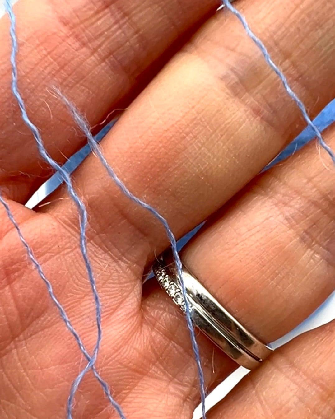 Hand wearing a silver ring with blue thread woven through the fingers