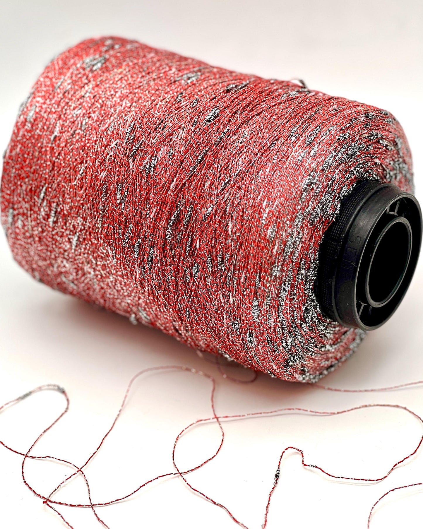 Spool of red thread with silver specks on a white background