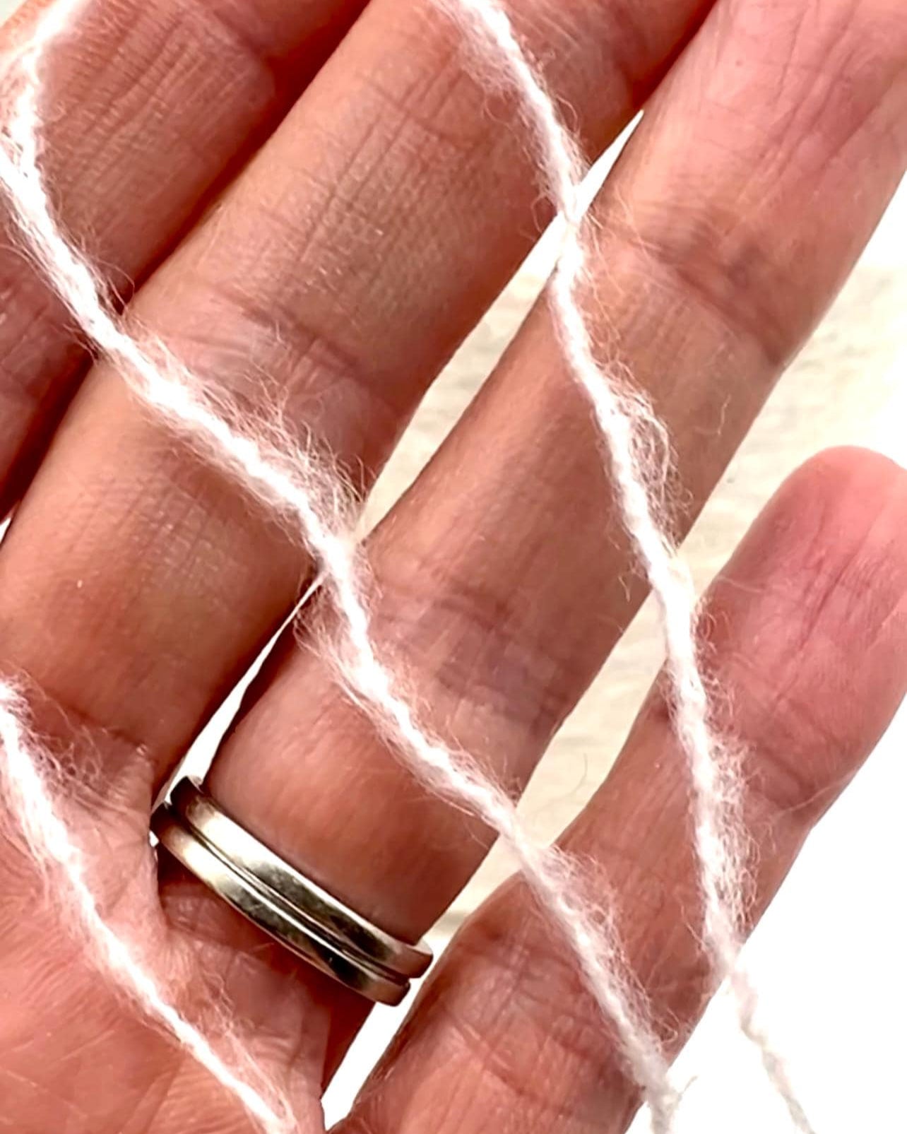 Hand wearing a silver ring with white fibers in the background
