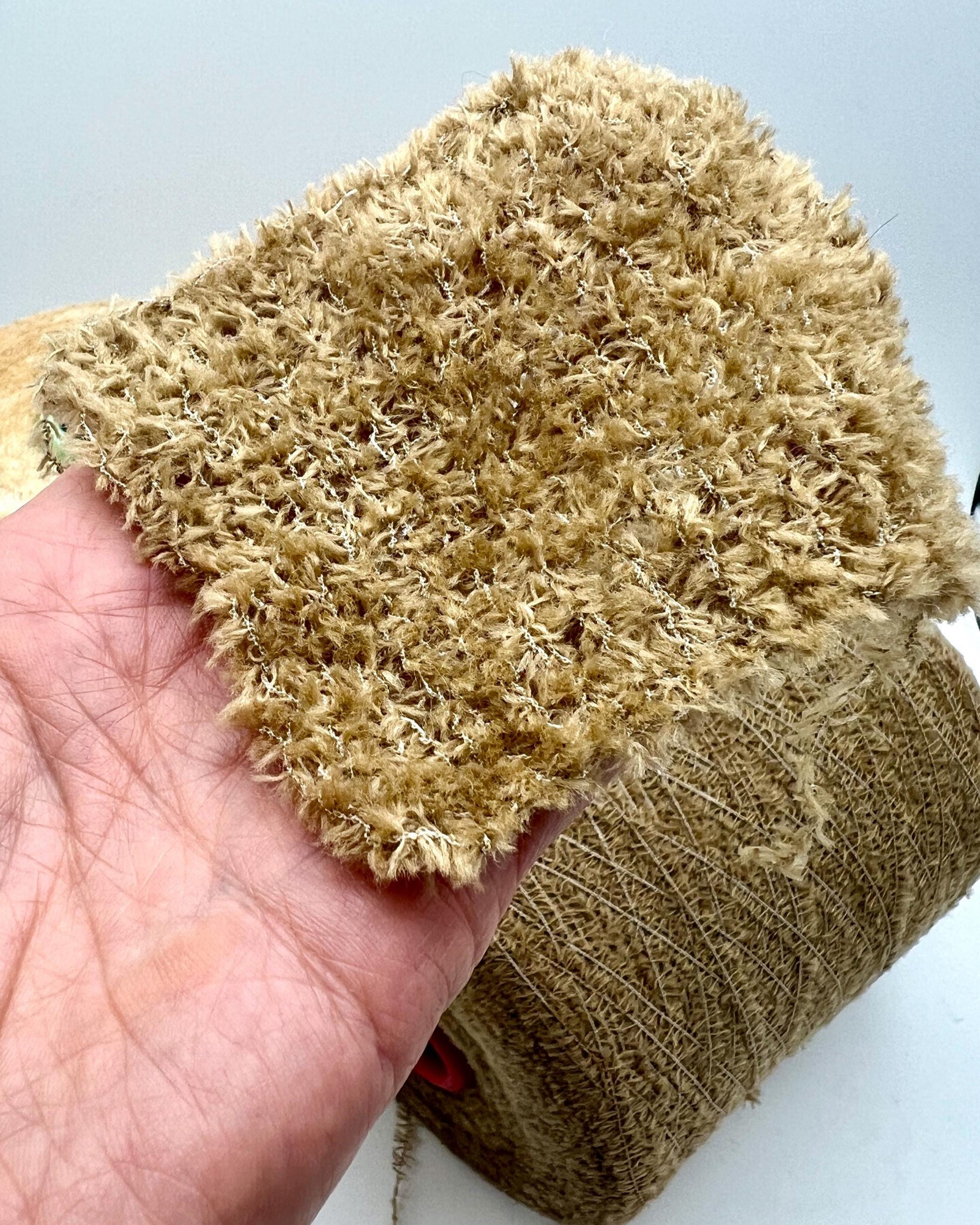 Hand holding a piece of textured beige fabric against a light background
