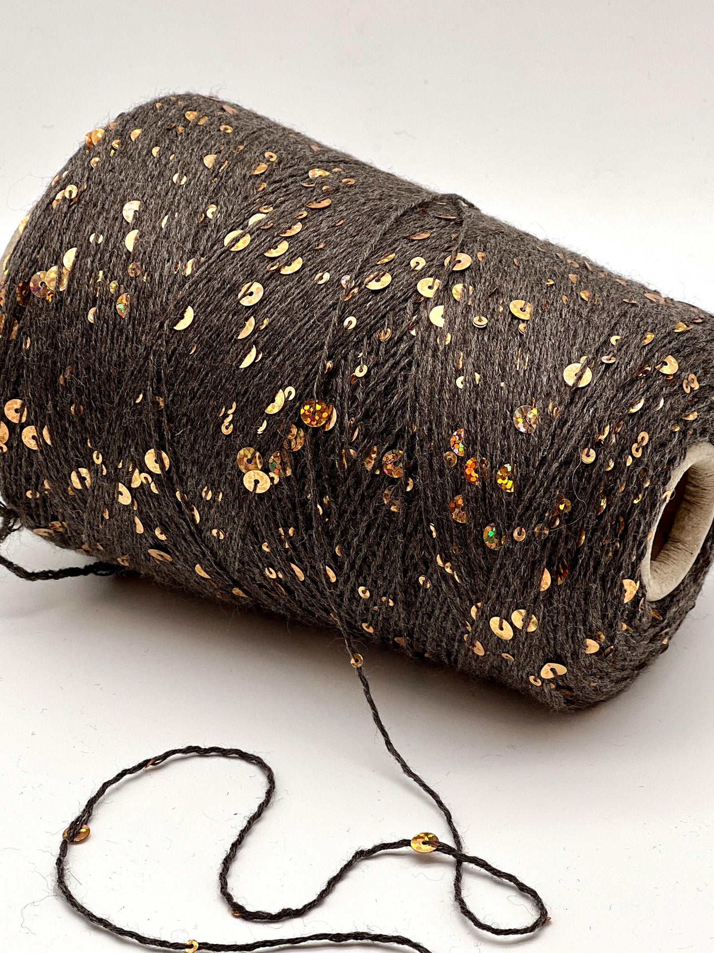 Roll of dark brown yarn with gold sequins on a white background