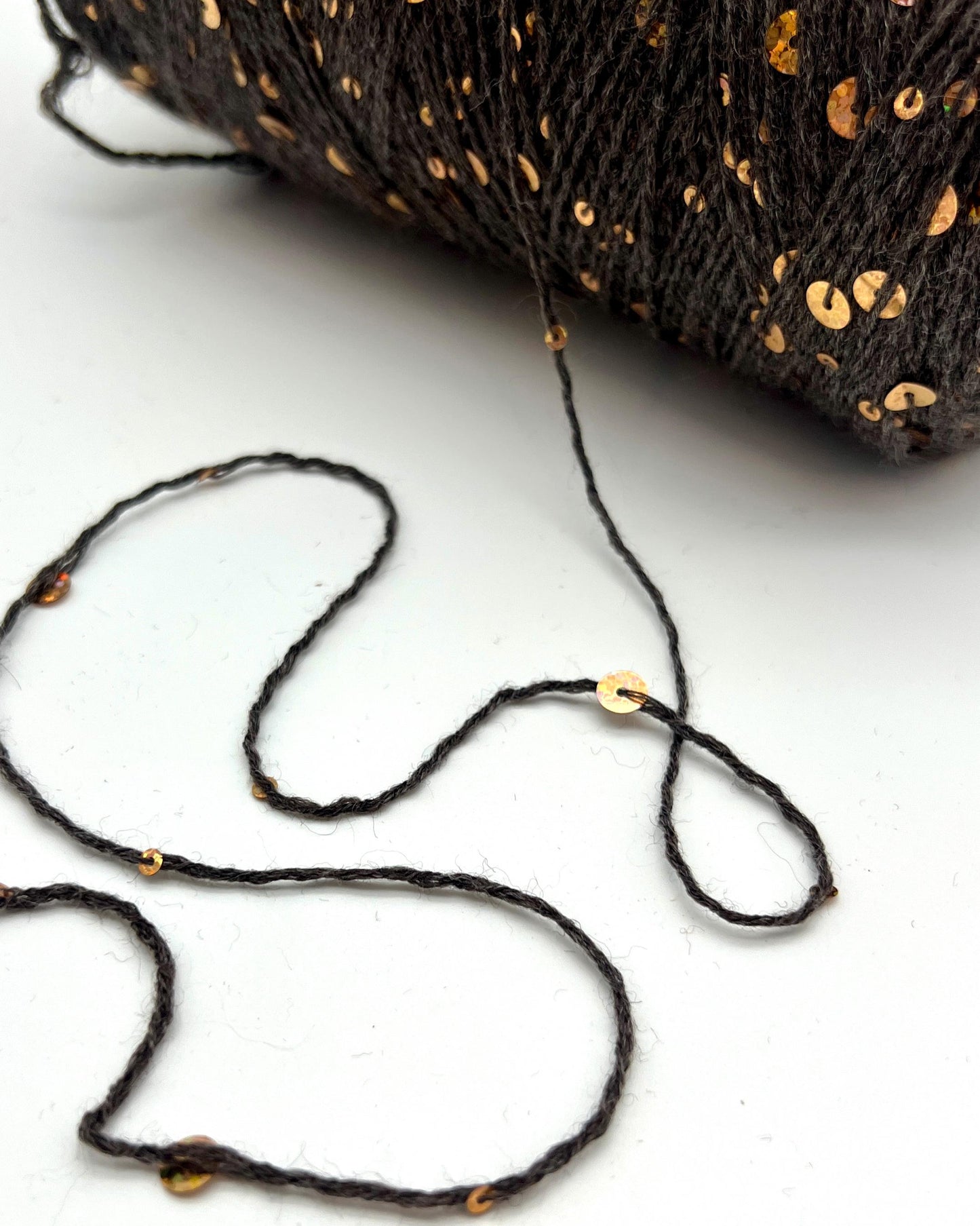 Spool of black thread with gold beads on a white background