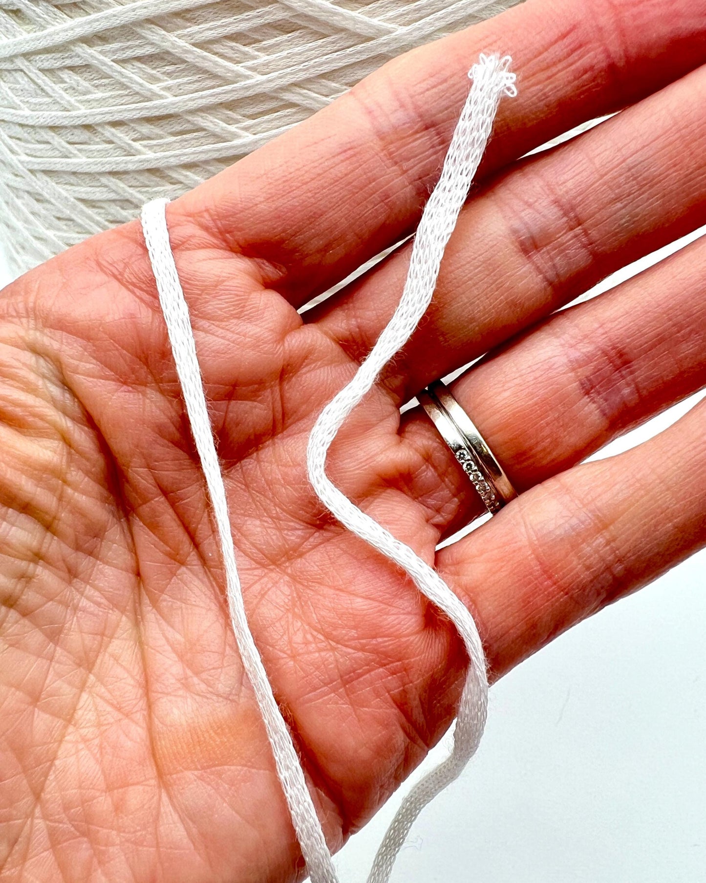 Hand holding a piece of white thread with a silver ring featuring engraved text.