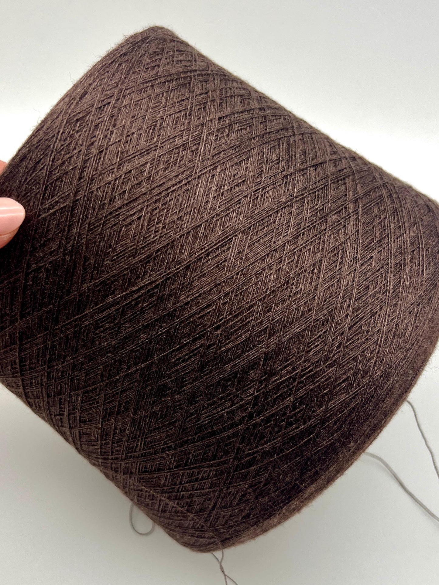 Brown yarn ball held by a hand on a white background