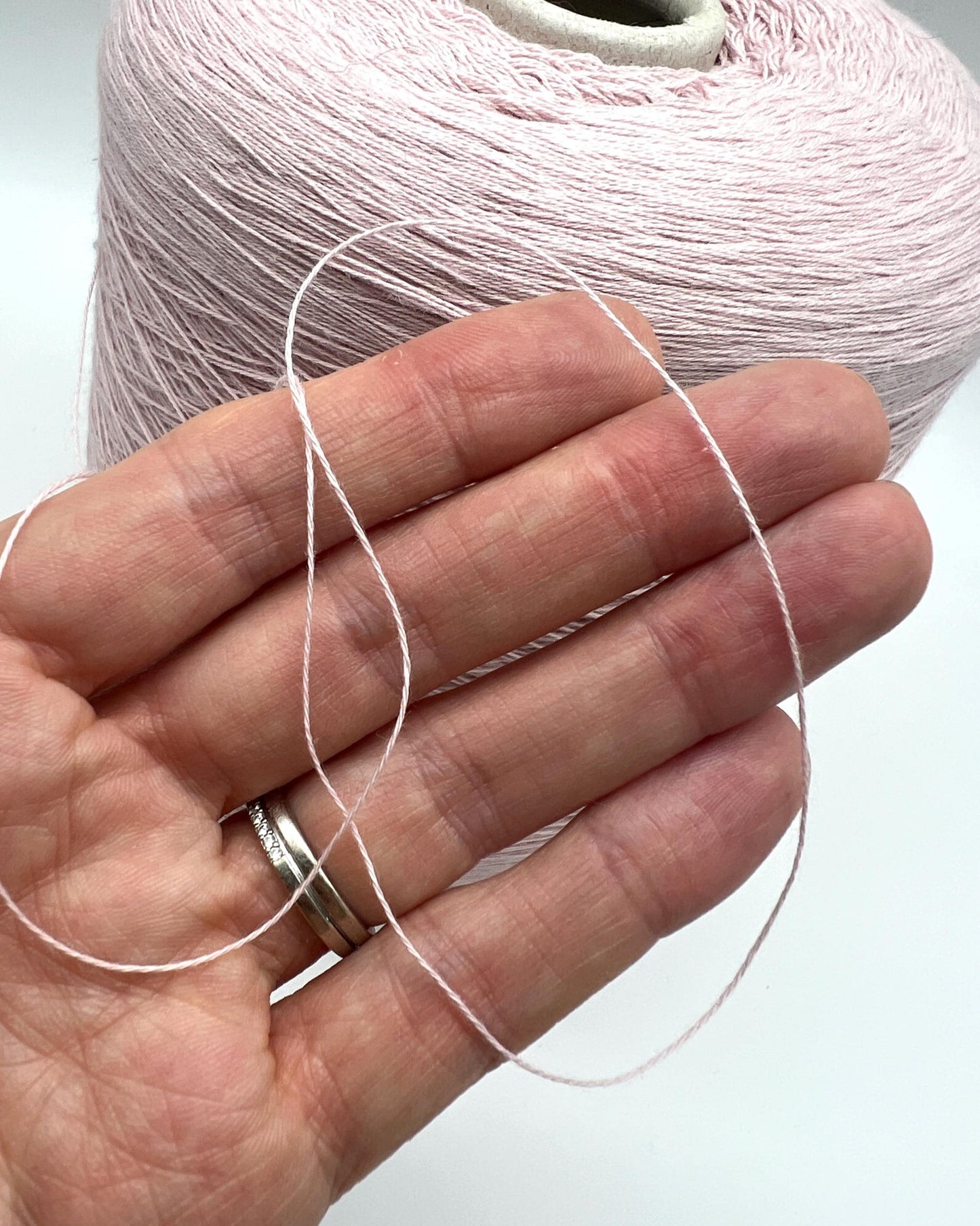 Hand holding a thread with a spool of pink yarn in the background