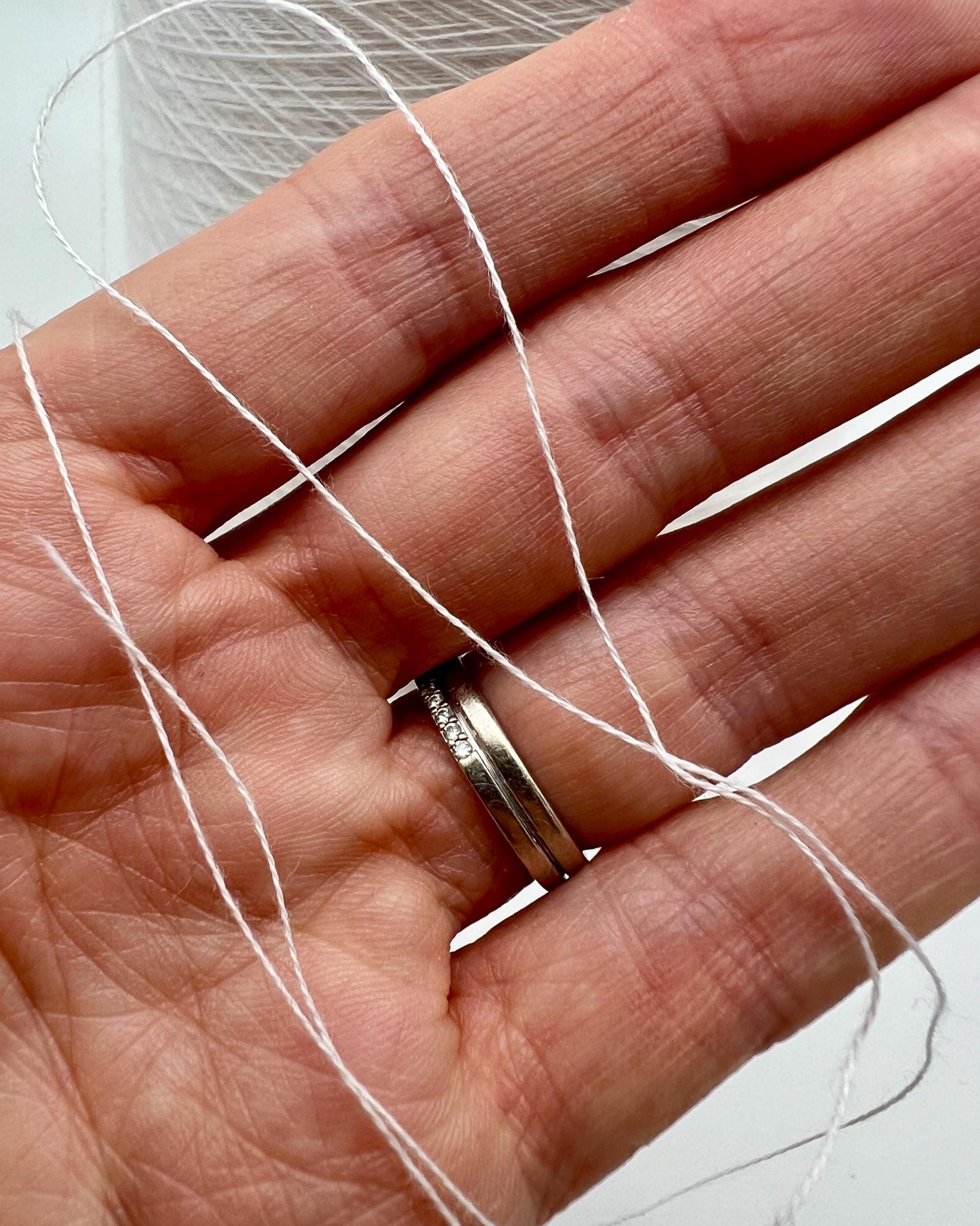 Hand holding a spool of white thread with a silver ring on a light background