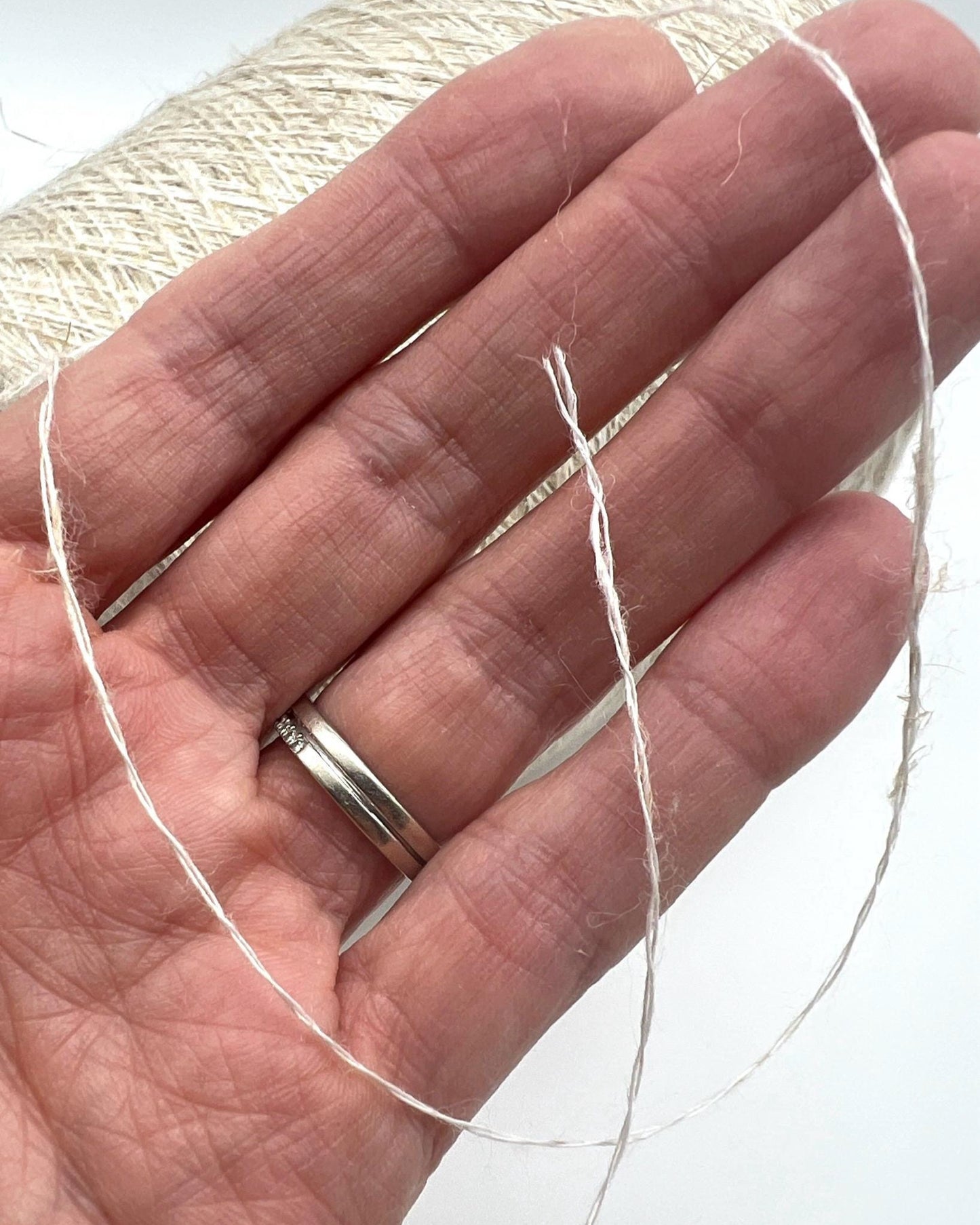 Hand holding a thread with a silver ring on a white background