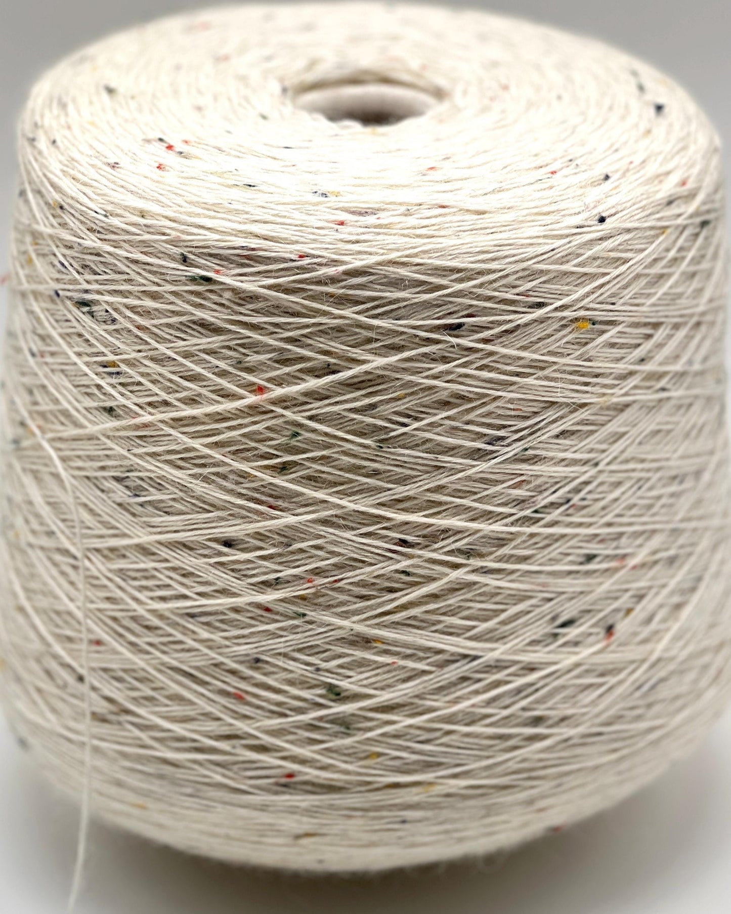 Spool of white yarn with specks on a gray background
