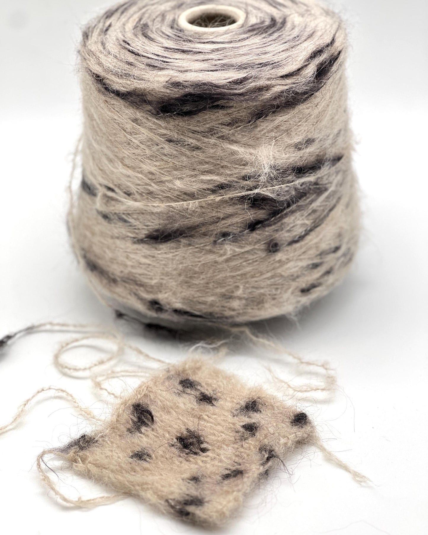 Spool of beige yarn with black speckles on a white background