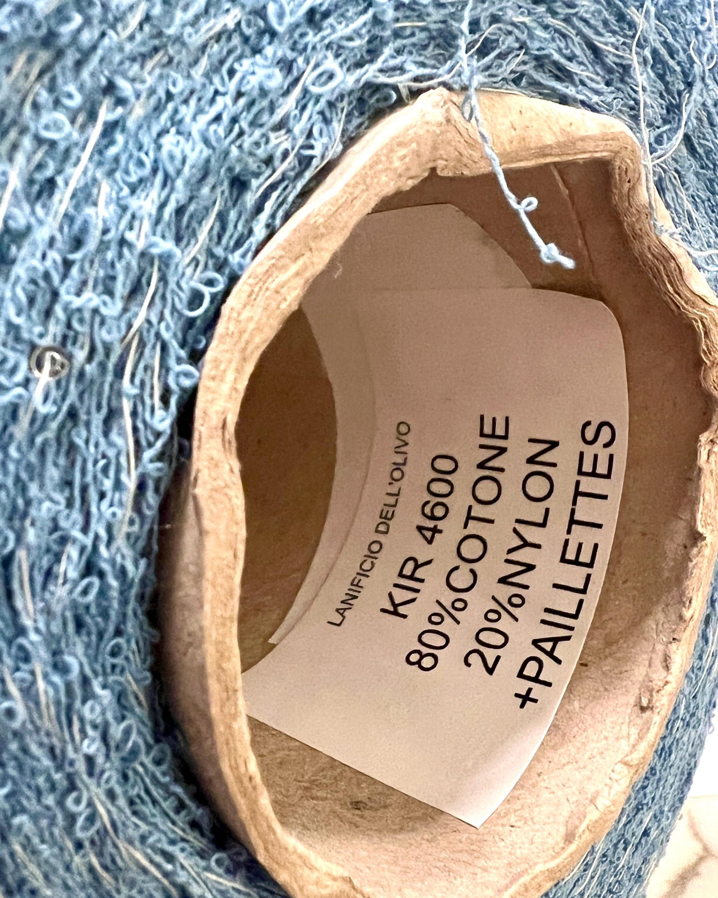 Yarn ball with a label indicating material composition on a blue yarn background