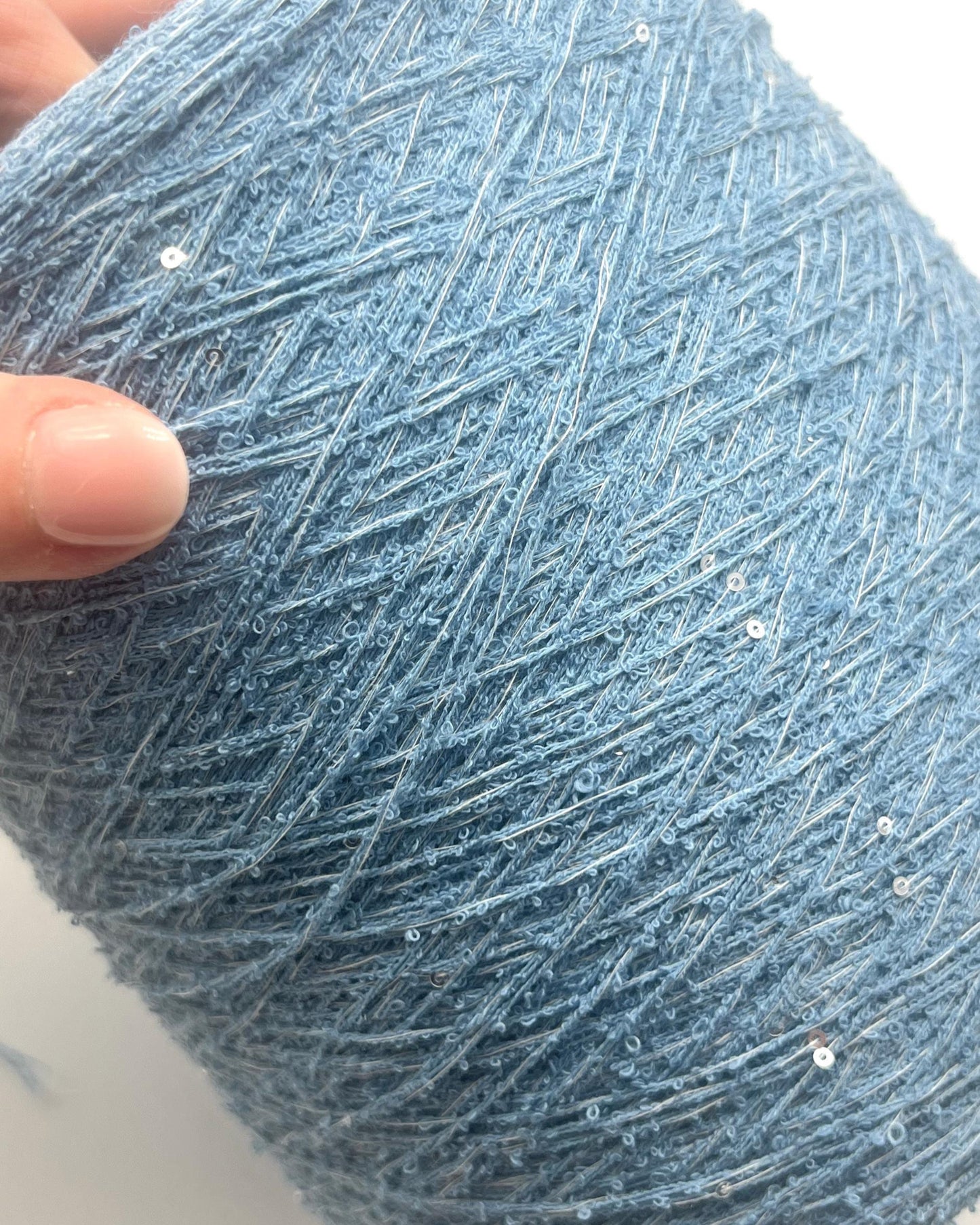 Close-up of a blue yarn ball with a hand holding it on a white background