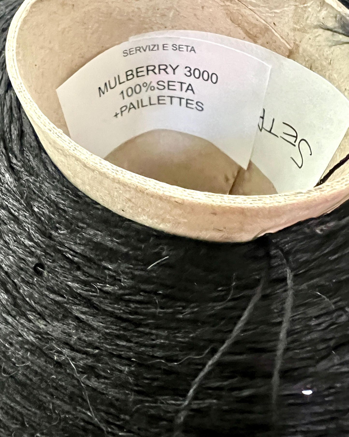 Spool of black yarn with a label on a wooden reel