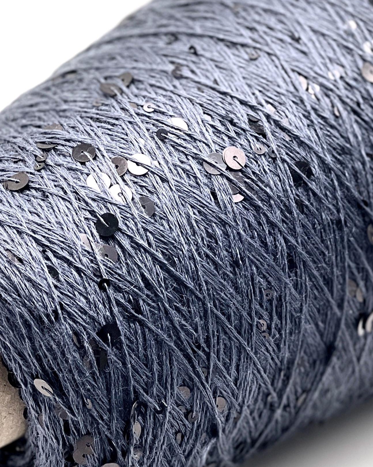Close-up of a roll of dark blue fabric with silver sequins on a light gray background