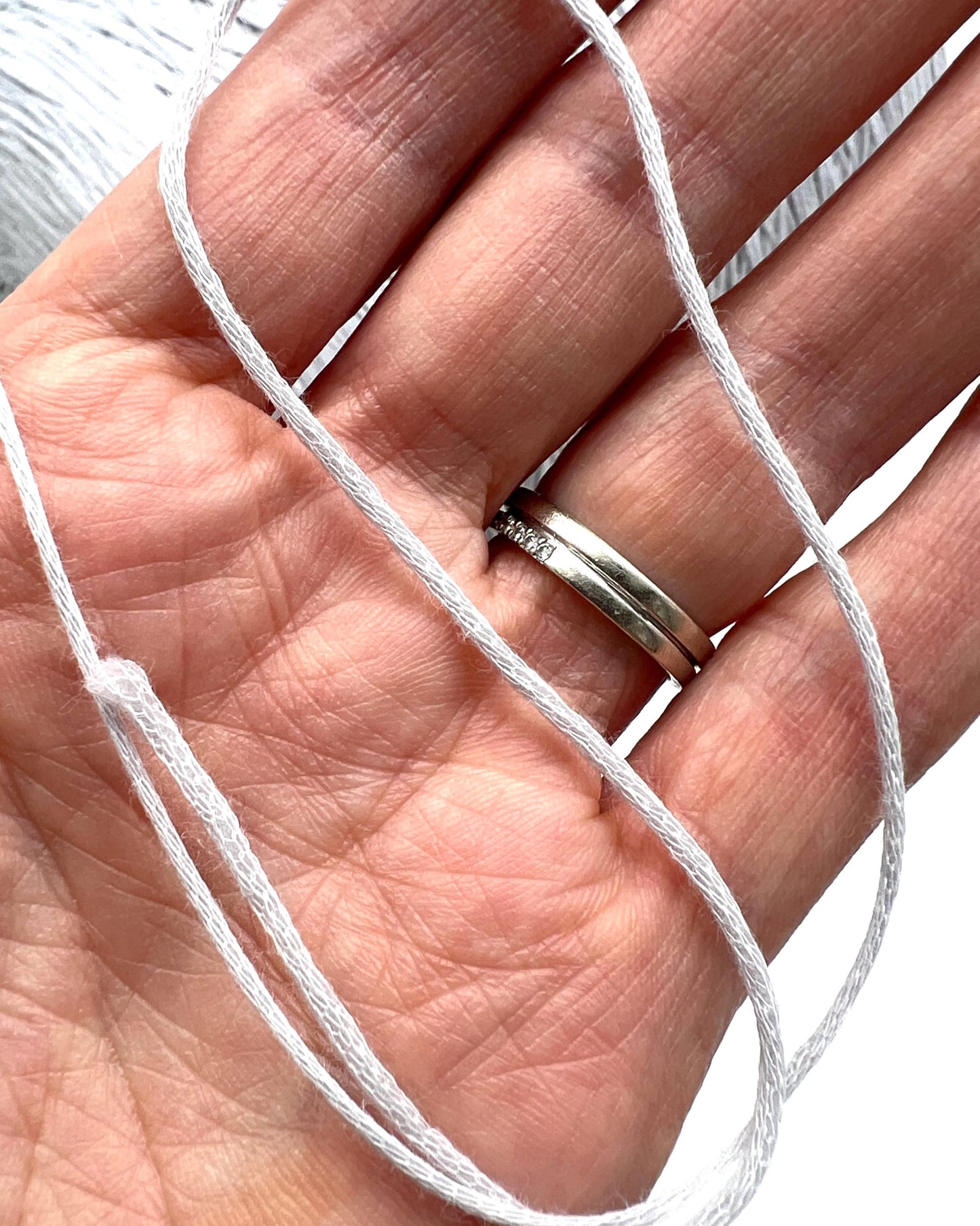 Hand holding a white thread with a silver ring on a neutral background