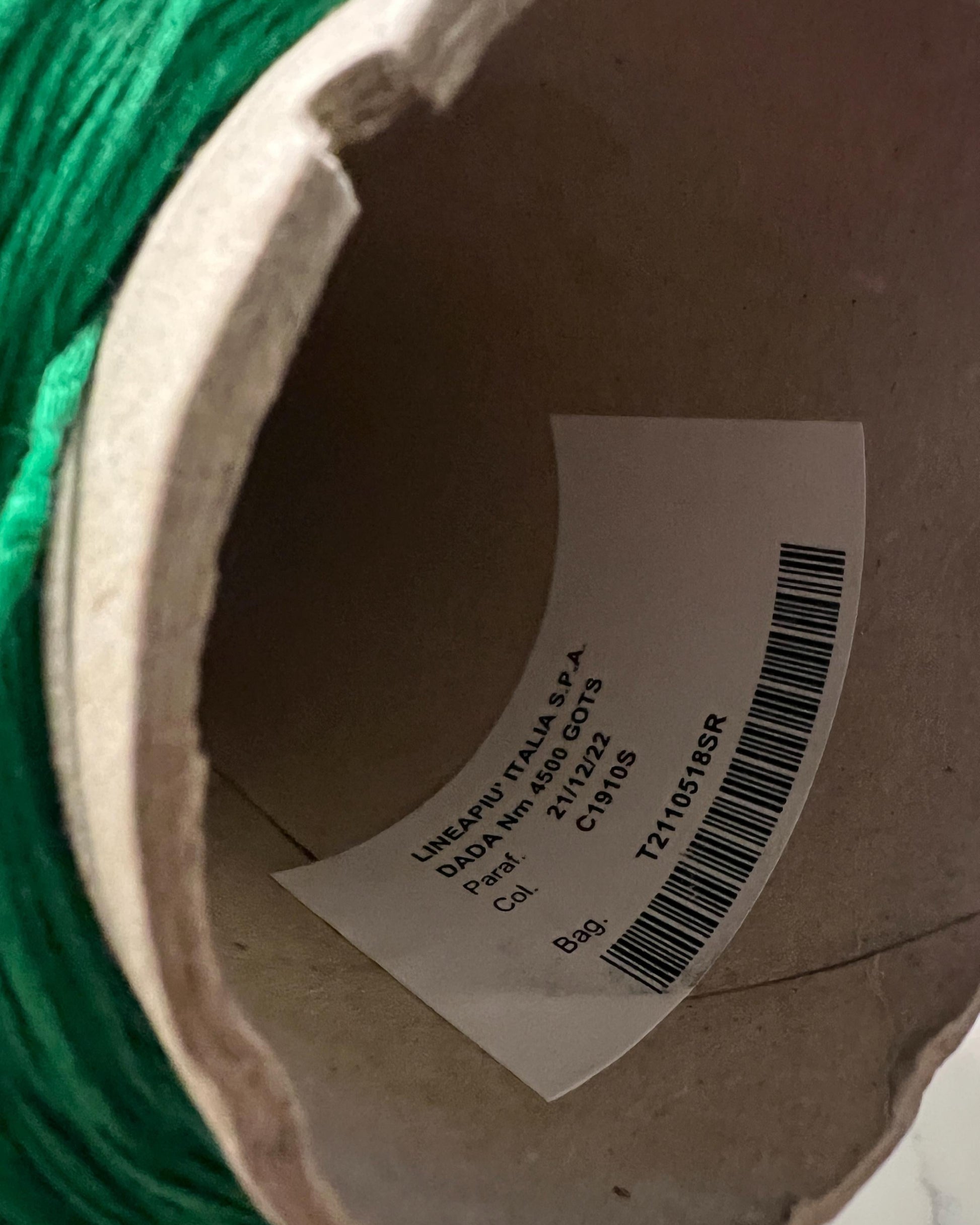 Close-up of a spool of green thread with a label on a cardboard background