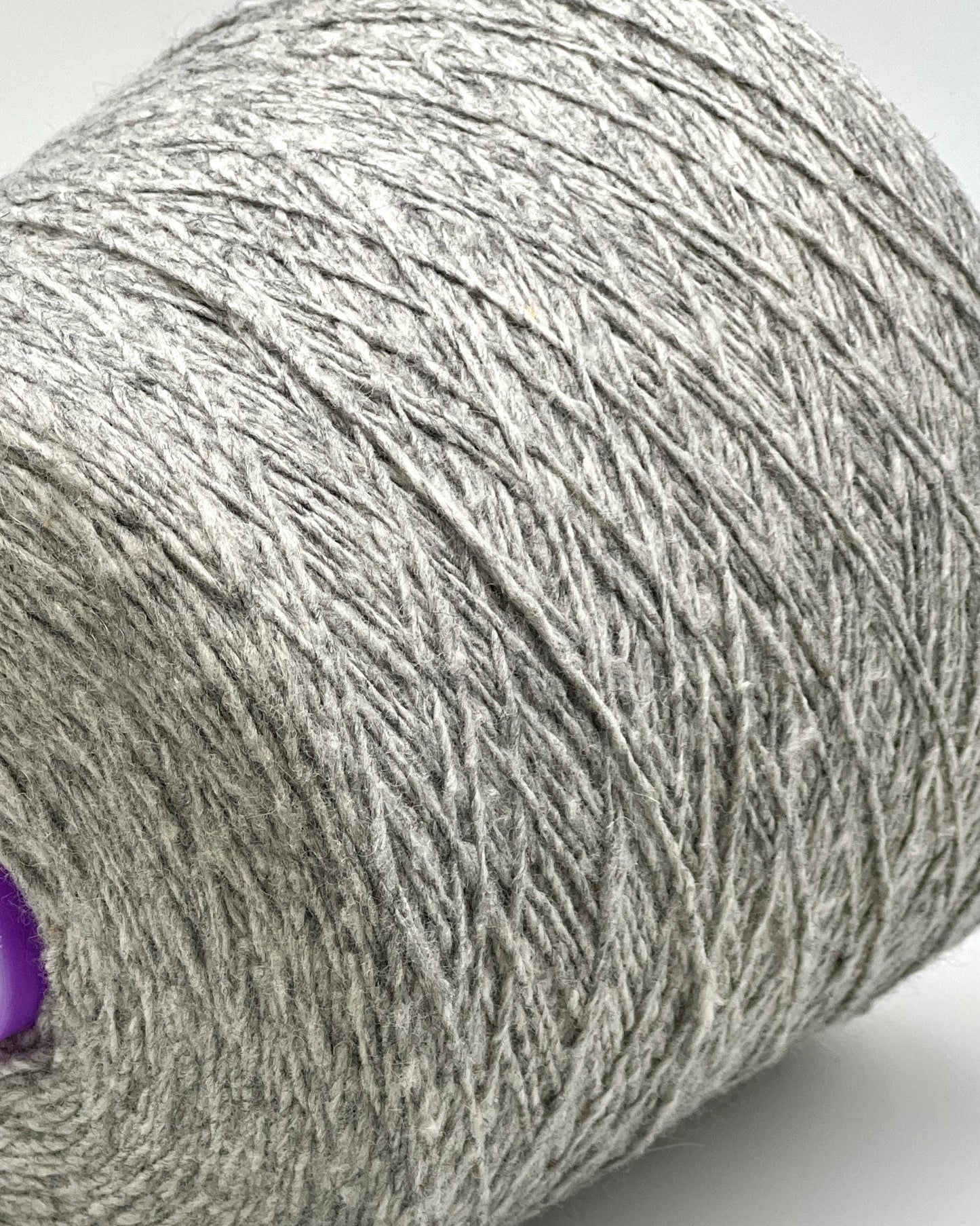 Close-up of a roll of gray yarn with a purple end on a white background