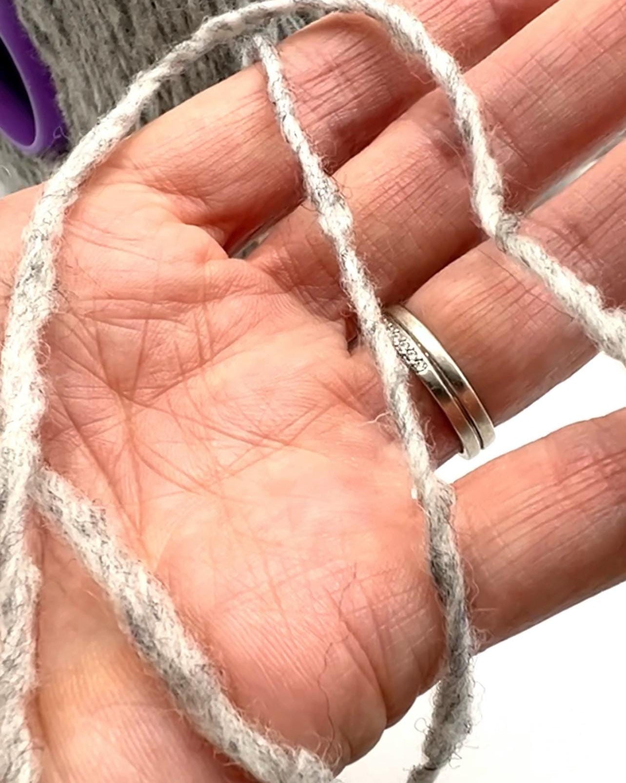 Hand holding a piece of white yarn with a blurred background