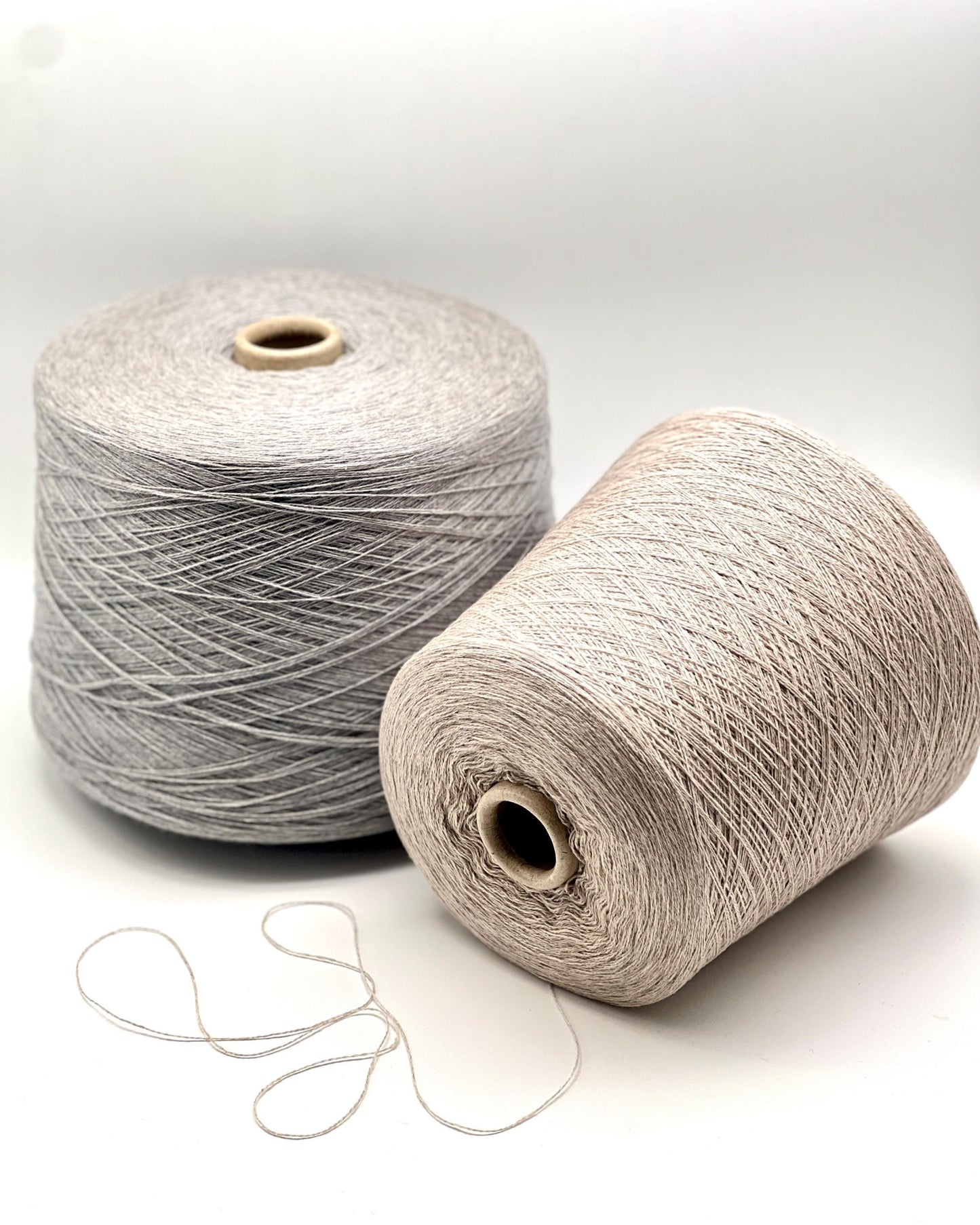 Two spools of yarn, one gray and one beige, on a white background.