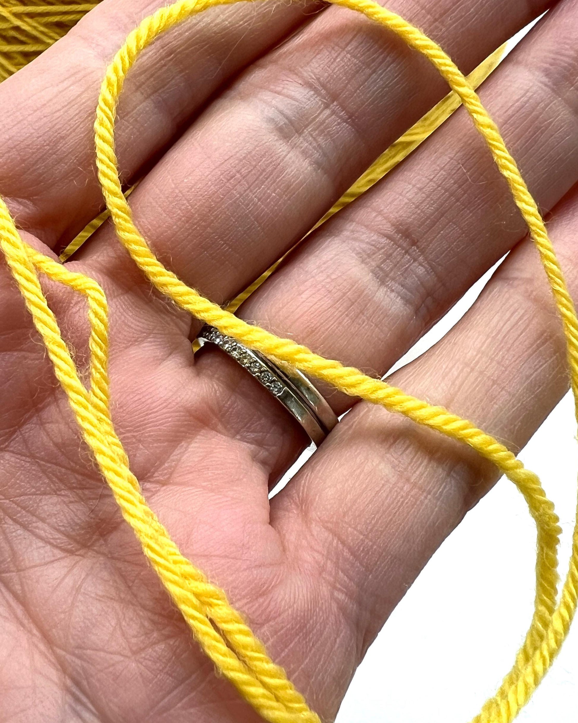 Hand holding a silver ring with yellow thread wrapped around it on a white background