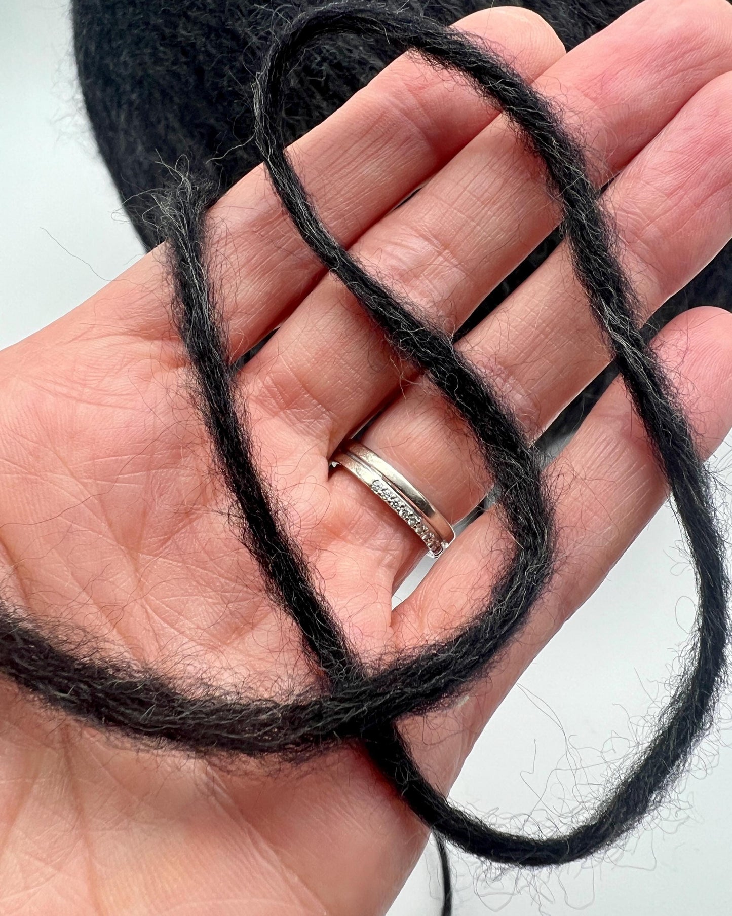 Black yarn held in a hand with a white background
