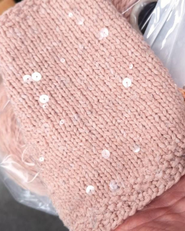 Pink knitted item with sequins held by a hand, wrapped in clear plastic.