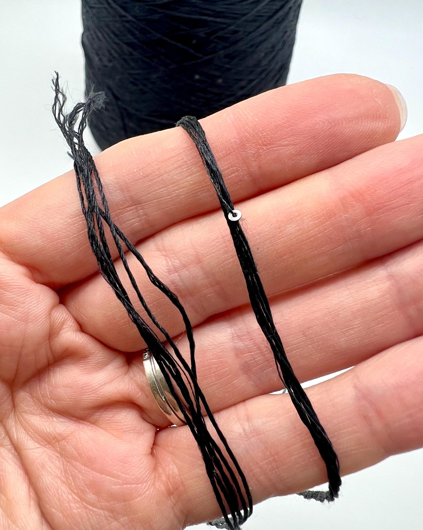 Black thread on a hand with a spool of thread in the background