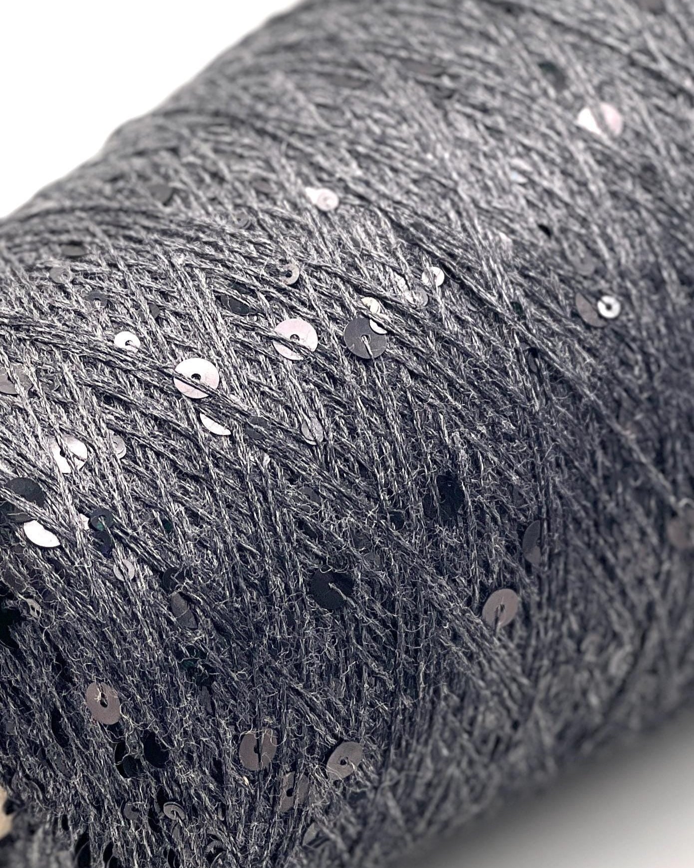 Close-up of a roll of dark gray fabric with sequins on a white background