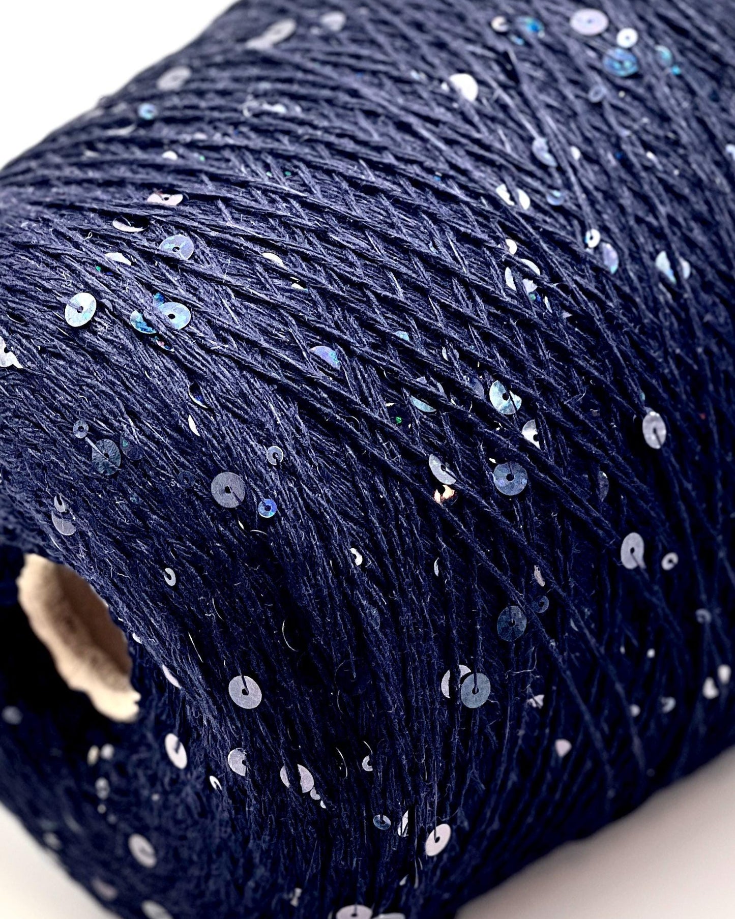 Close-up of a roll of dark blue yarn with small white and silver sequins on a light background.