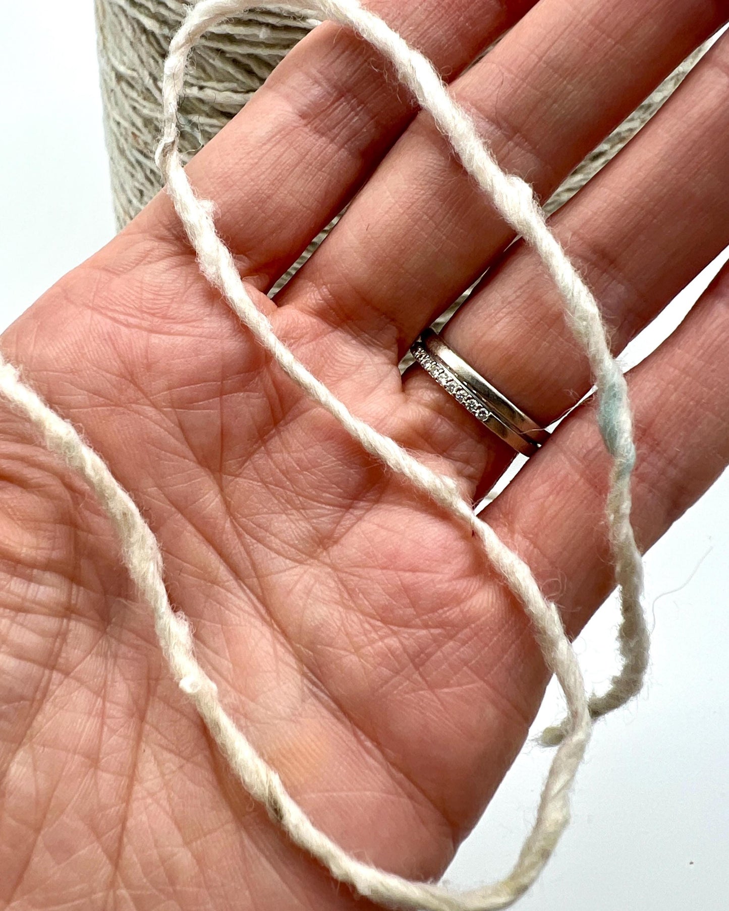 Hand holding a ball of white yarn with a blurred background