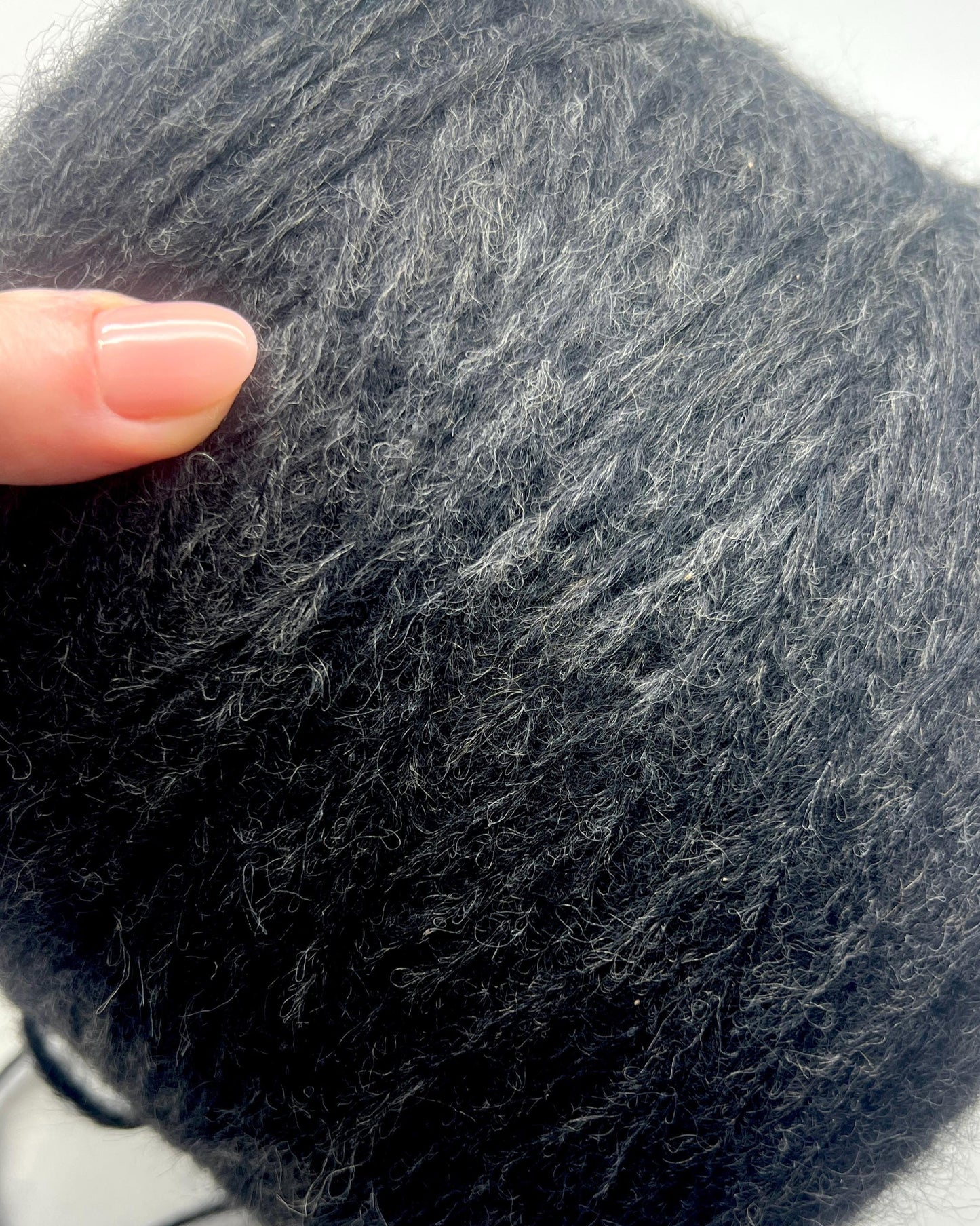 Close-up of a dark gray yarn ball with a hand touching it
