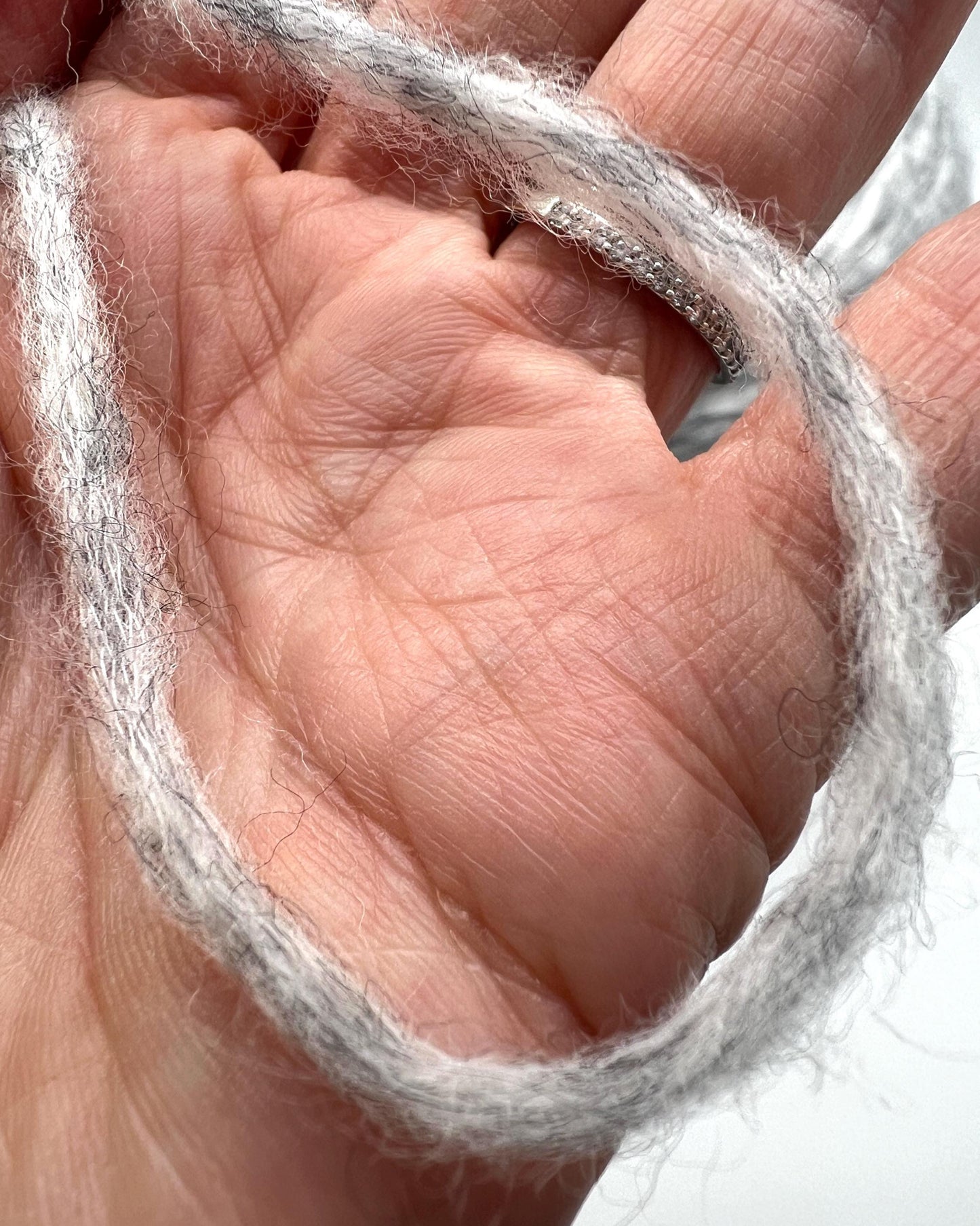 Close-up of a hand holding a ball of gray yarn.