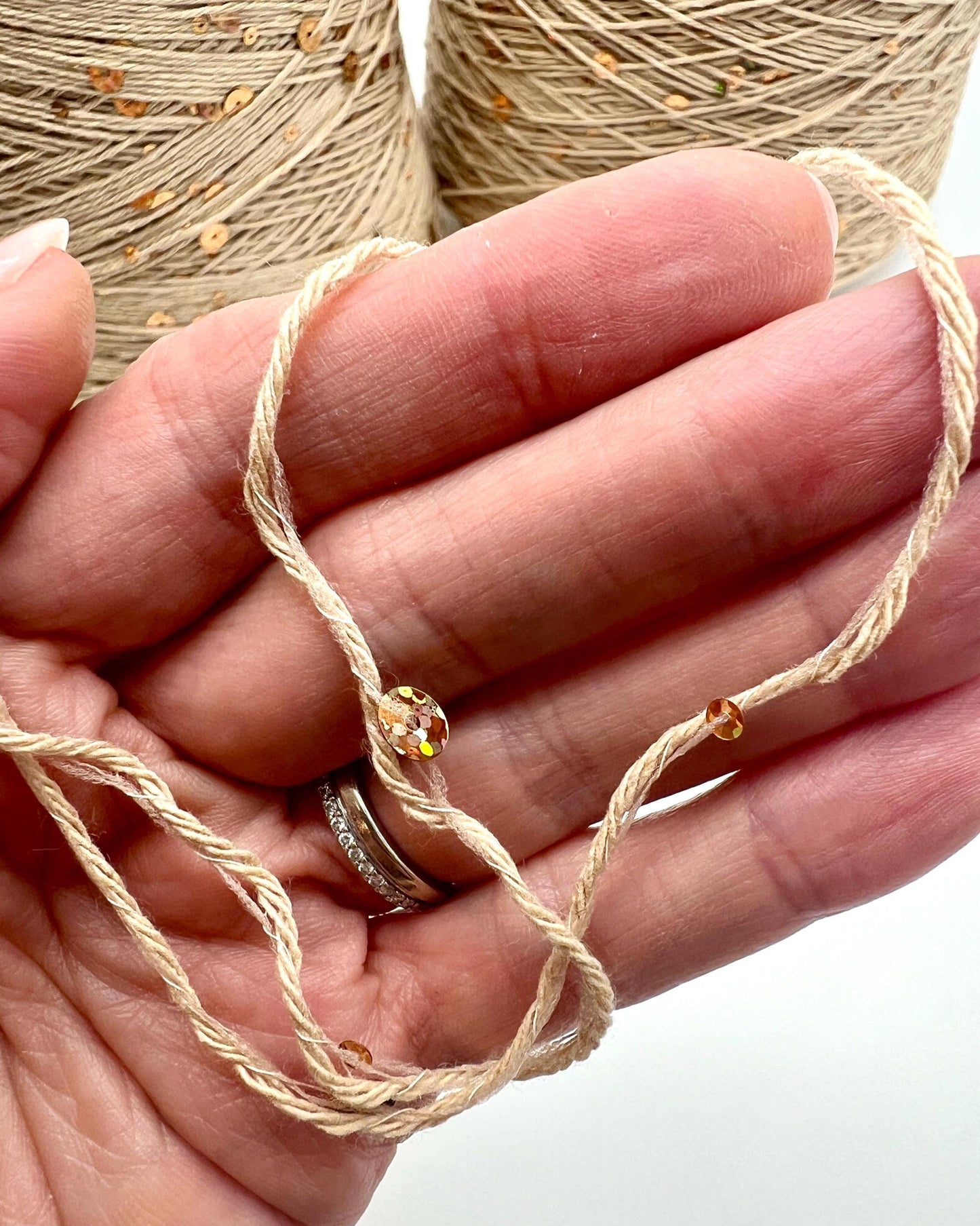 Hand holding beige thread with a spool in the background