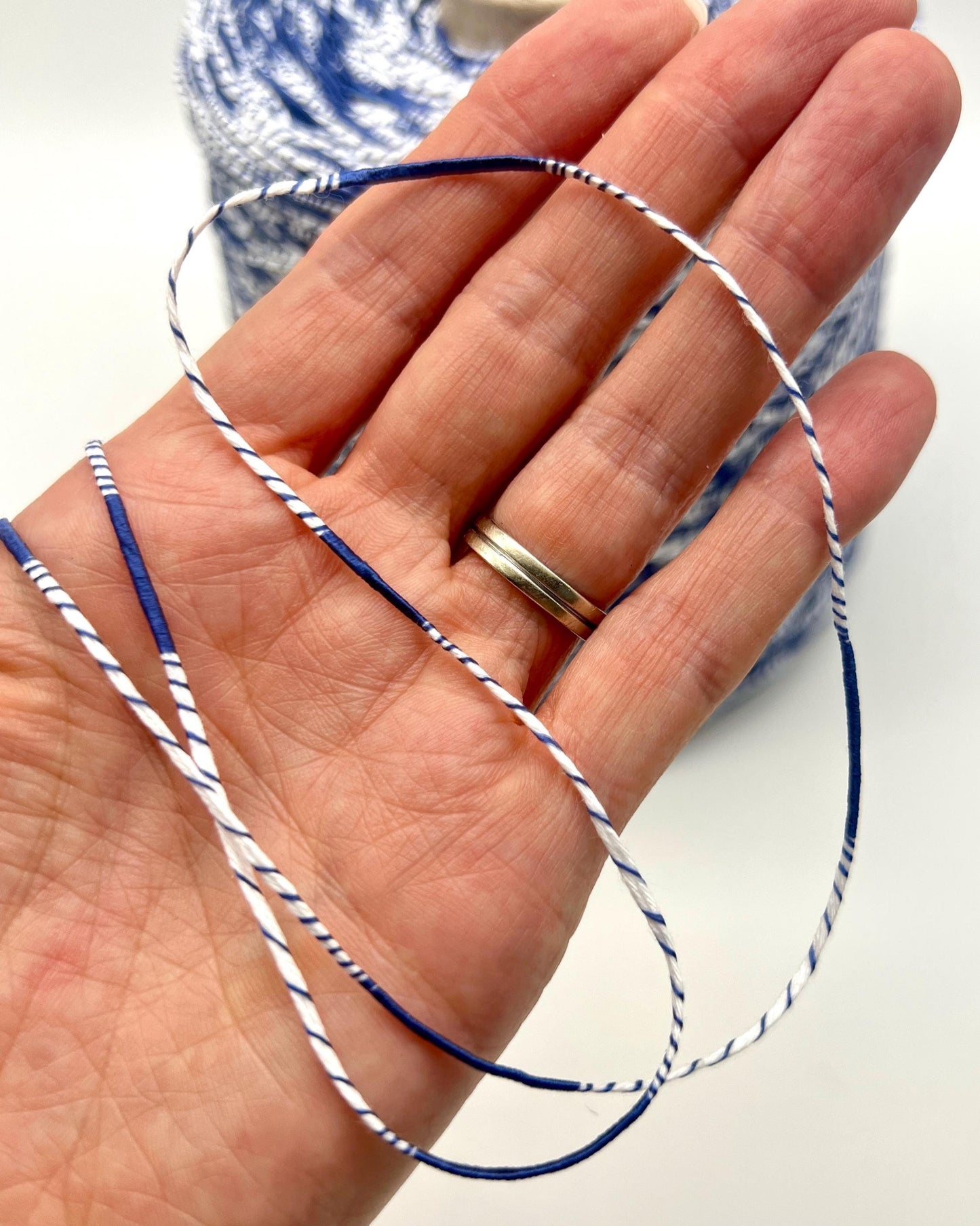 Hand holding blue and white string with spool in background