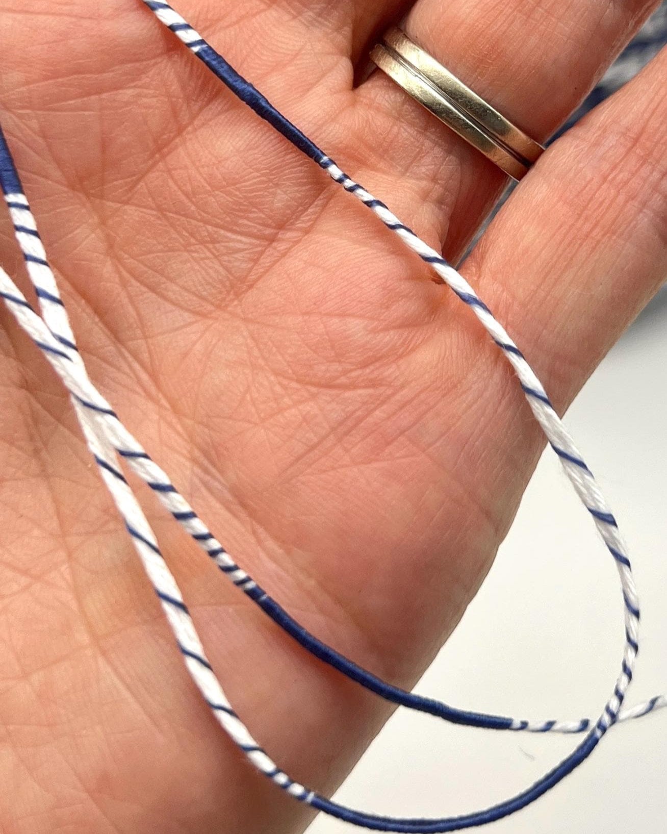 Hand holding a blue and white string with a gold ring on a blurred background