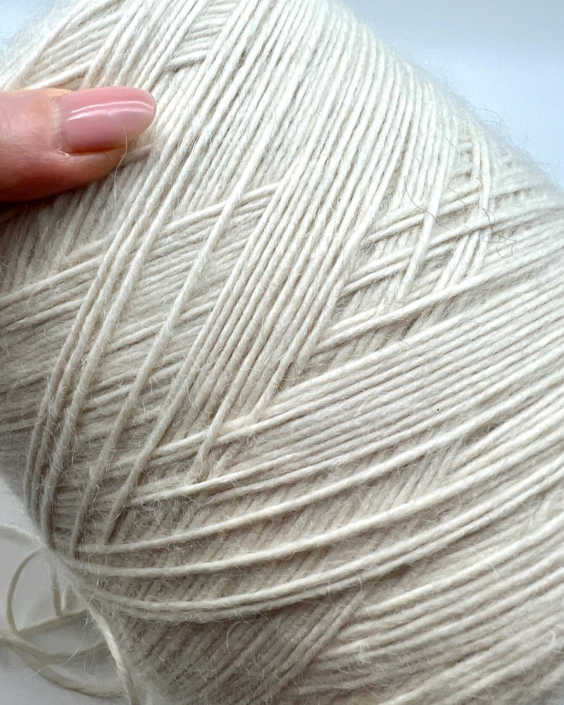 Close-up of a ball of white yarn with a hand holding it.