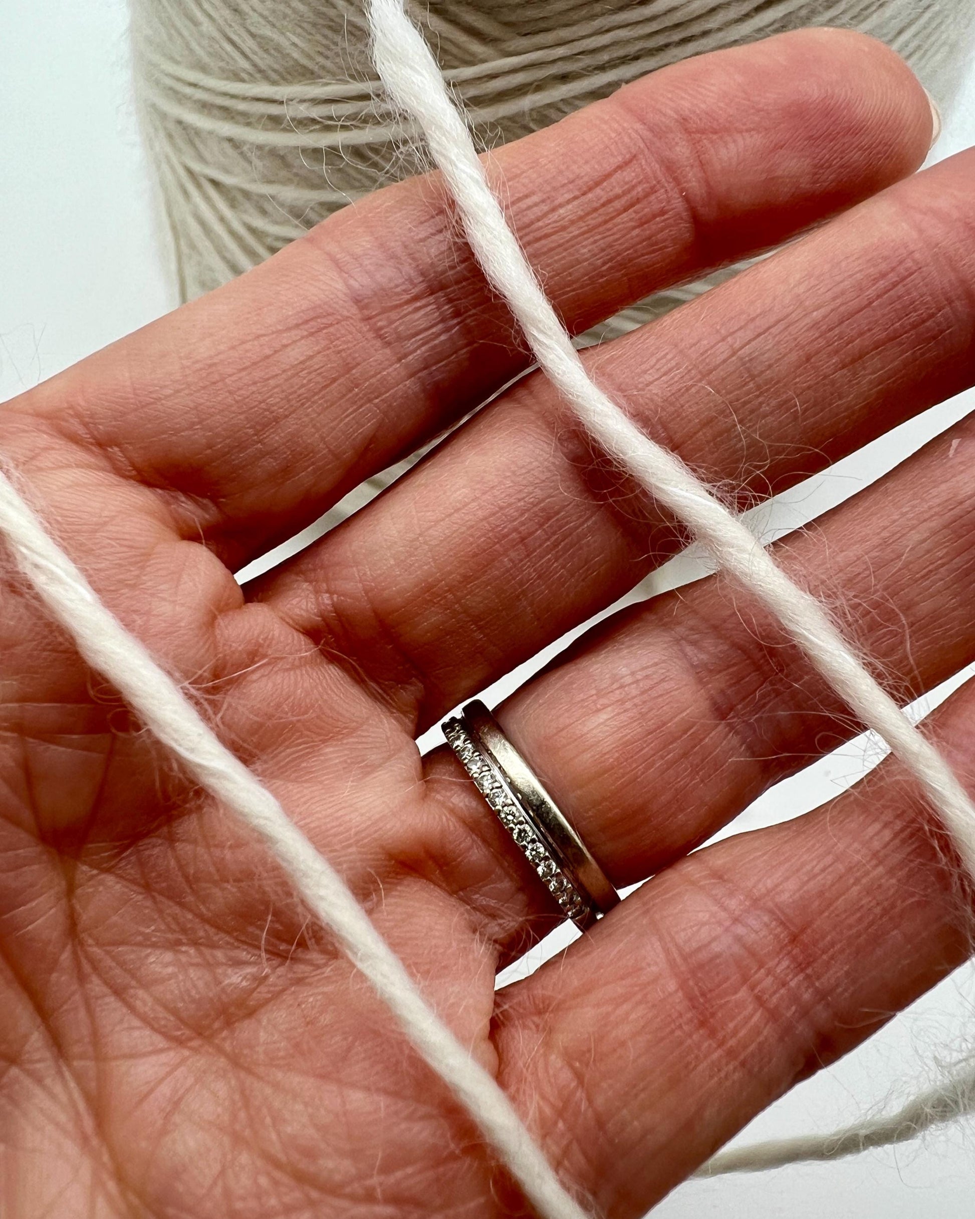 Hand holding white yarn with a close-up of the yarn and hand.