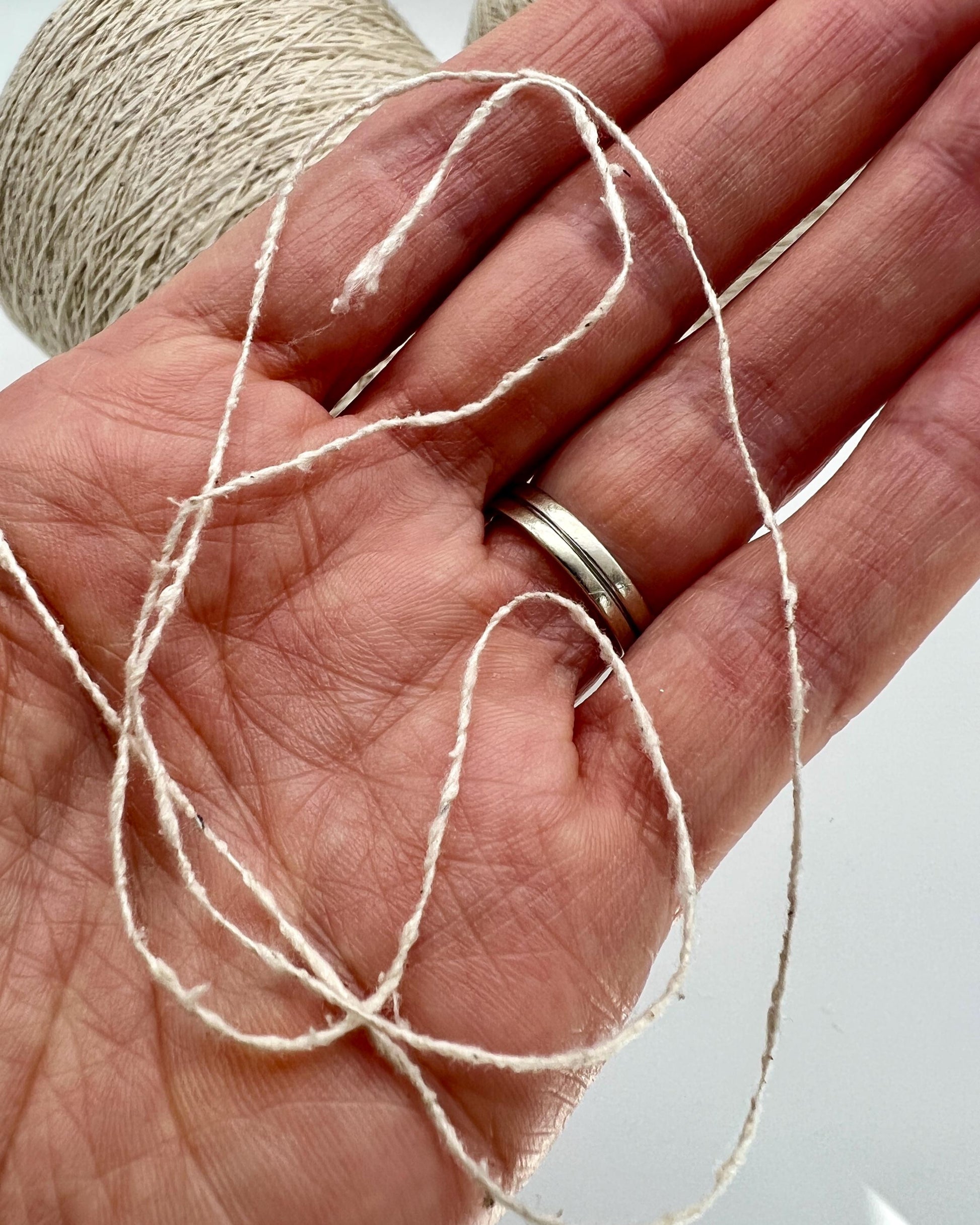 Hand holding a ball of beige yarn with a plain background