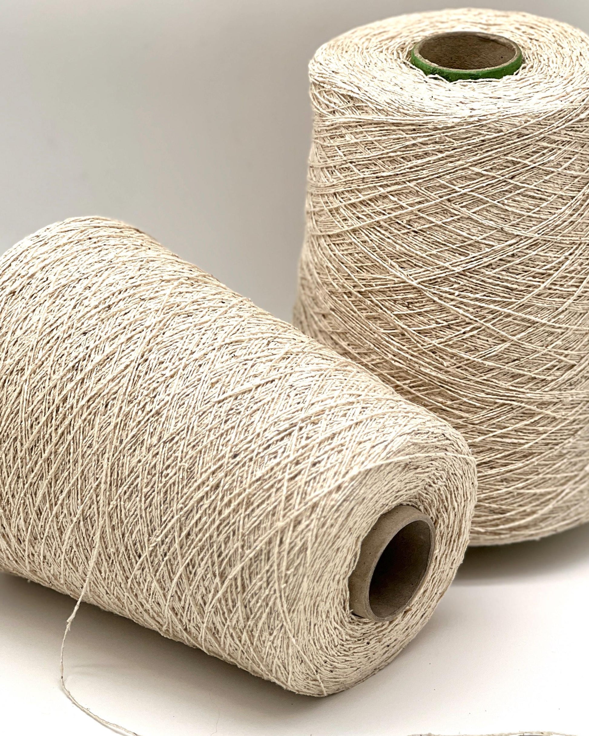 Two spools of beige thread on a light gray background