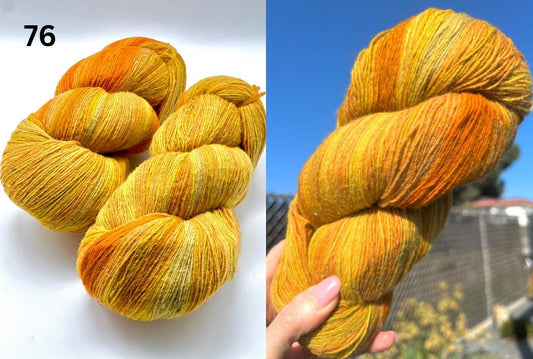 Two skeins of orange and yellow yarn on a white background, with one skein held in a hand against a blue sky.