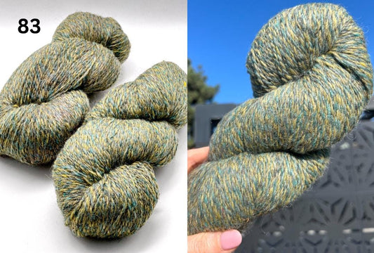 Green and brown skein of yarn on a white background, held in hand with blue sky in the background.