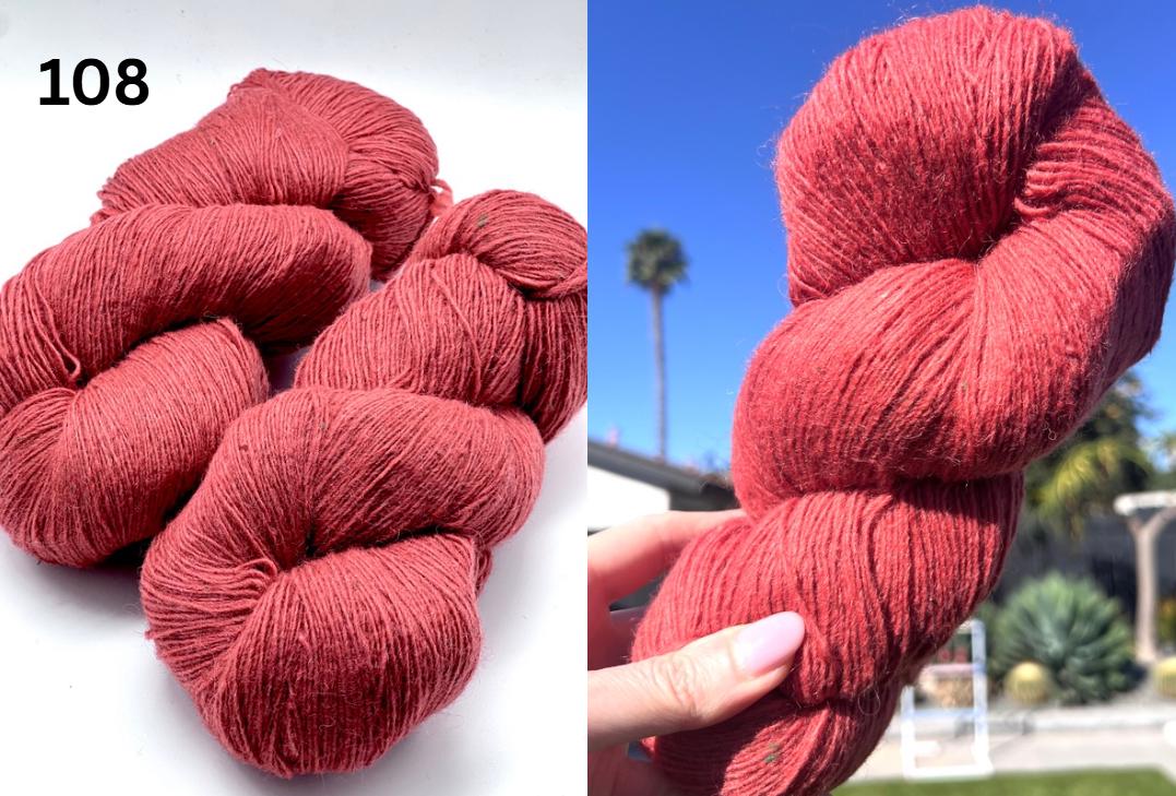 Red yarn skeins with a hand holding one, set against a blue sky with palm trees.