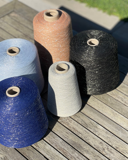 A luxurious cone of Pecci Filati SHIMMER yarn, a modern 50% Cotton, 25% Linen, 14% Polyester, and 12% Polyamide (Lurex) blend. The image showcases the refined metallic glow and delicate texture of this 3400m/100g Italian extrafine yarn, ideal for high-end blending. Authentic luxury fiber available at iDOKNiT.com.