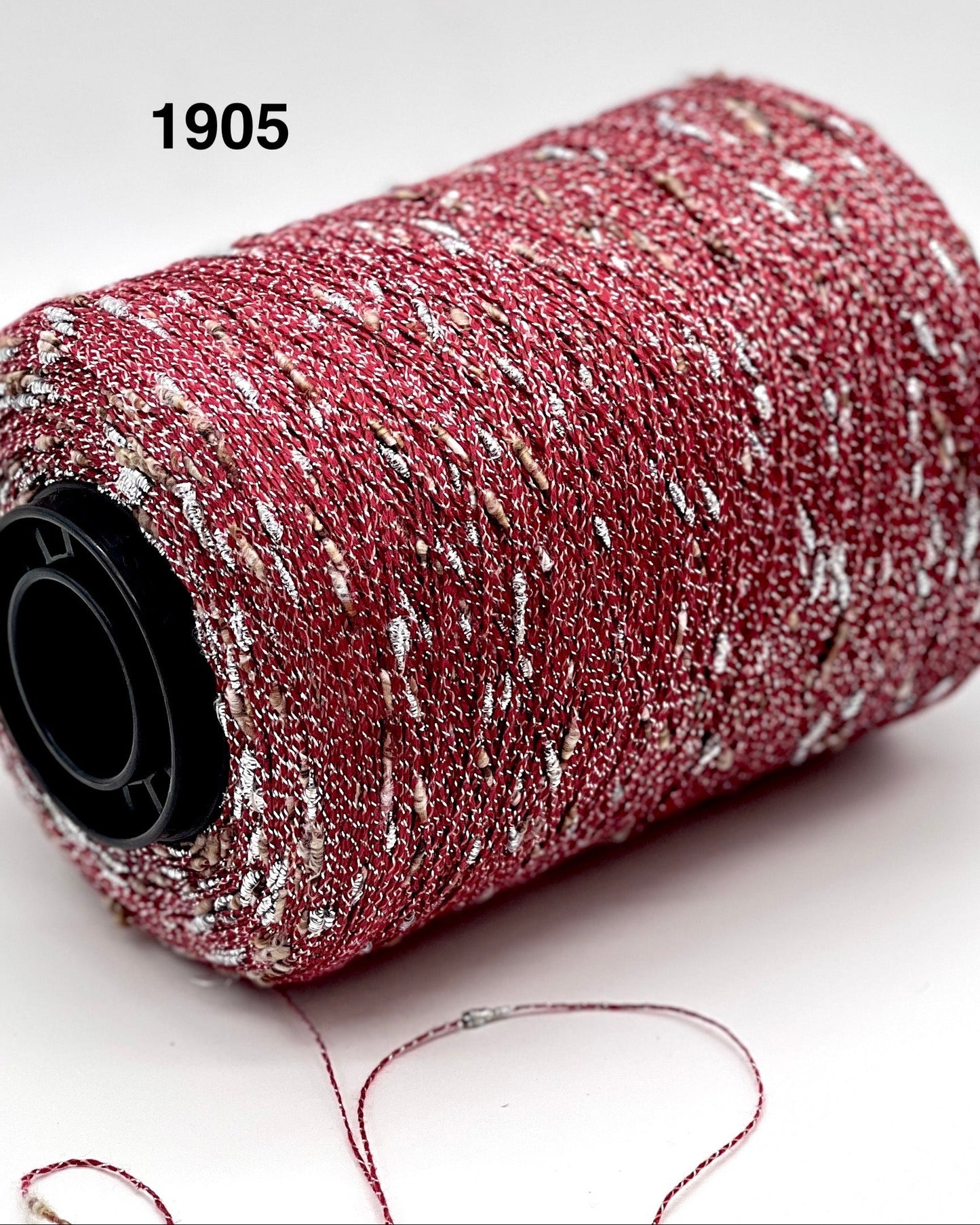 Red glittery spool of thread with a heart-shaped piece of thread on a white background
