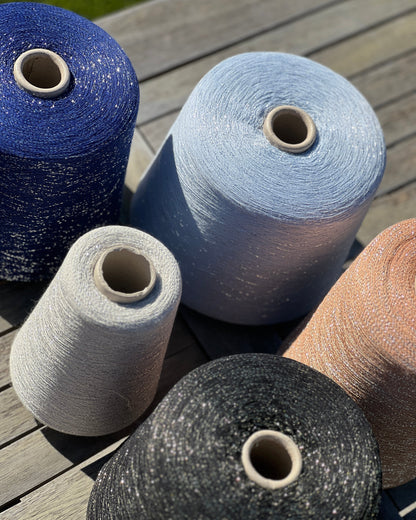 A luxurious cone of Pecci Filati SHIMMER yarn, a modern 50% Cotton, 25% Linen, 14% Polyester, and 12% Polyamide (Lurex) blend. The image showcases the refined metallic glow and delicate texture of this 3400m/100g Italian extrafine yarn, ideal for high-end blending. Authentic luxury fiber available at iDOKNiT.com.