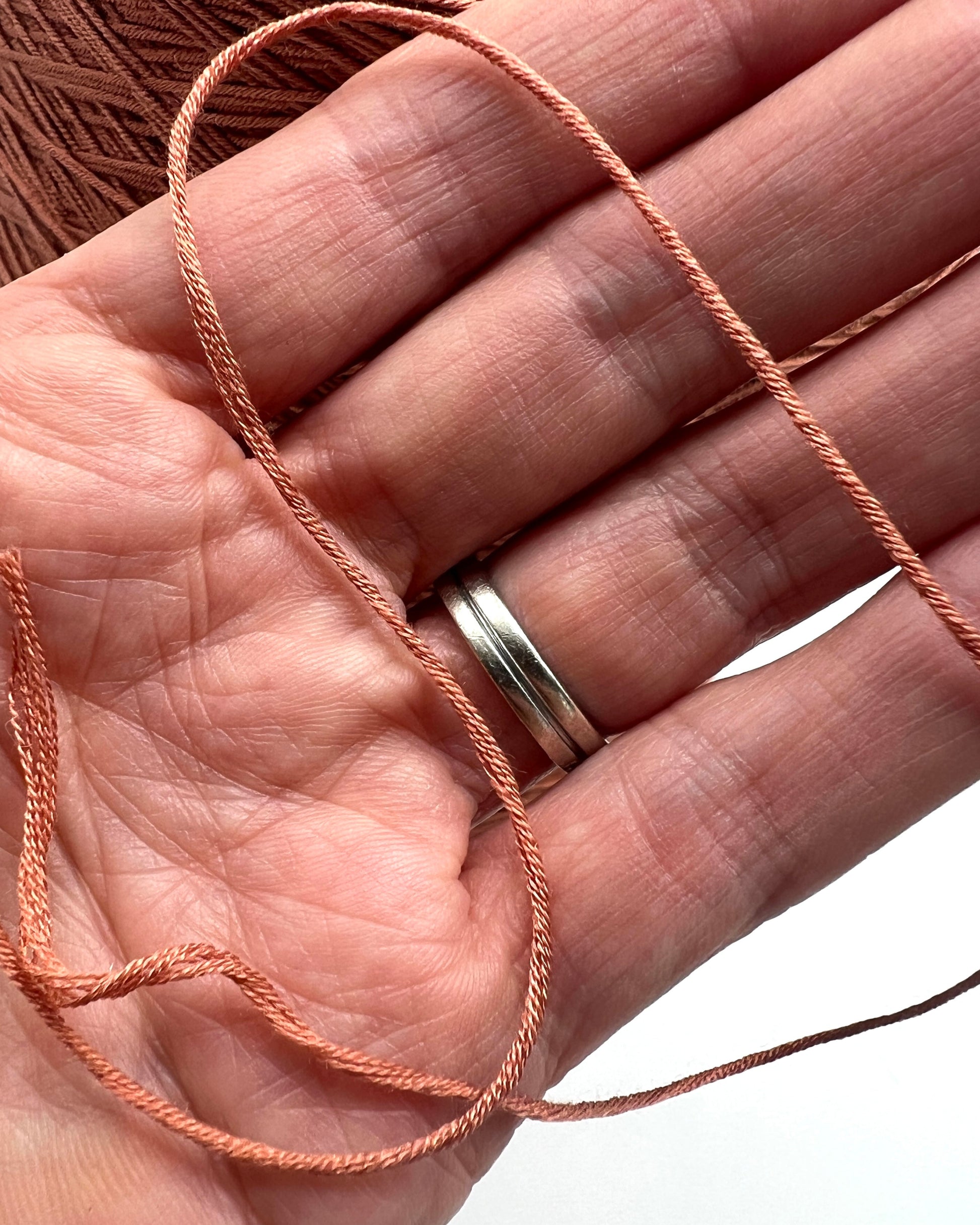 Hand holding pink thread with a silver ring on a white background